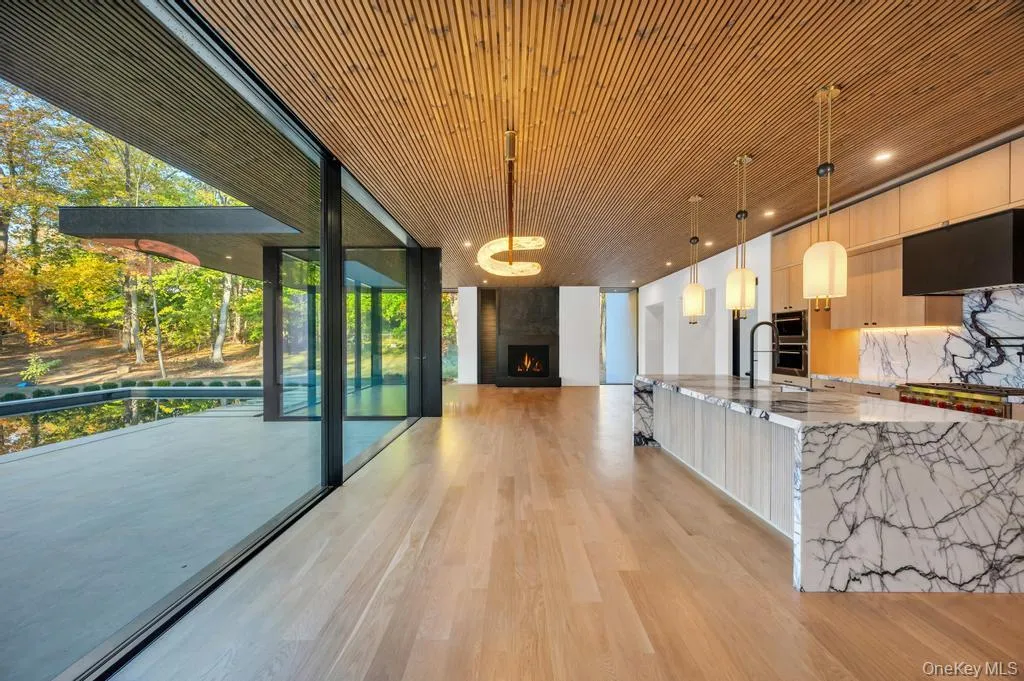 Kitchen featuring a wall of windows, hanging light fixtures, open floor plan, light stone counters, and a fireplace Kitchen featuring a wall of windows, hanging light fixtures, open floor plan, light stone counters, and a fireplace