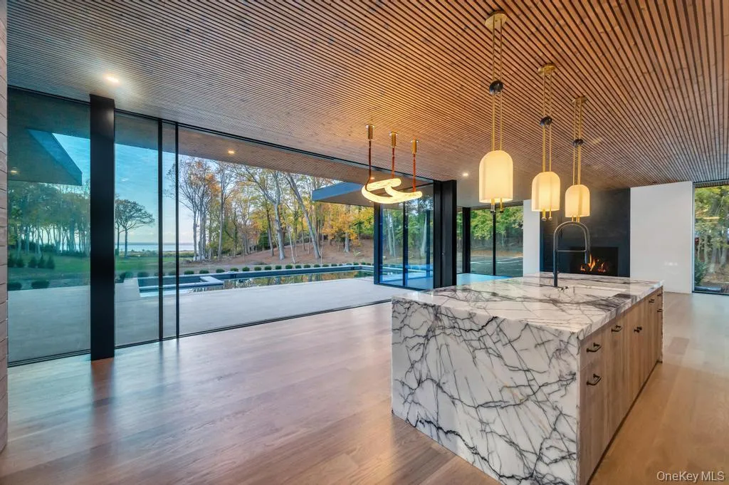 Kitchen with expansive windows, hanging light fixtures, light stone counters, light wood-type flooring, and a lit fireplace Kitchen with expansive windows, hanging light fixtures, light stone counters, light wood-type flooring, and a lit fireplace