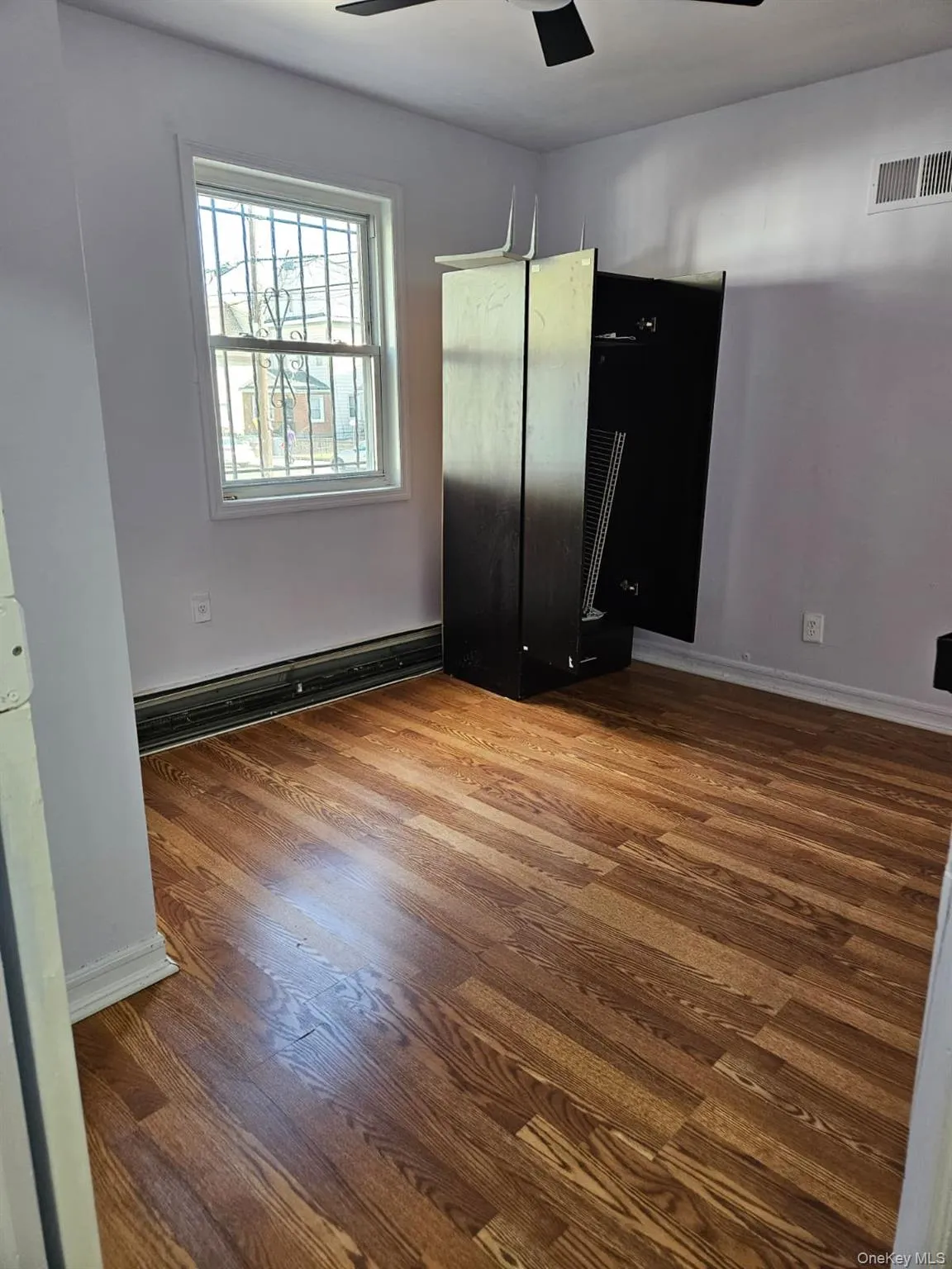 Unfurnished bedroom with wood finished floors, a ceiling fan, and a baseboard heating unit Unfurnished bedroom with wood finished floors, a ceiling fan, and a baseboard heating unit