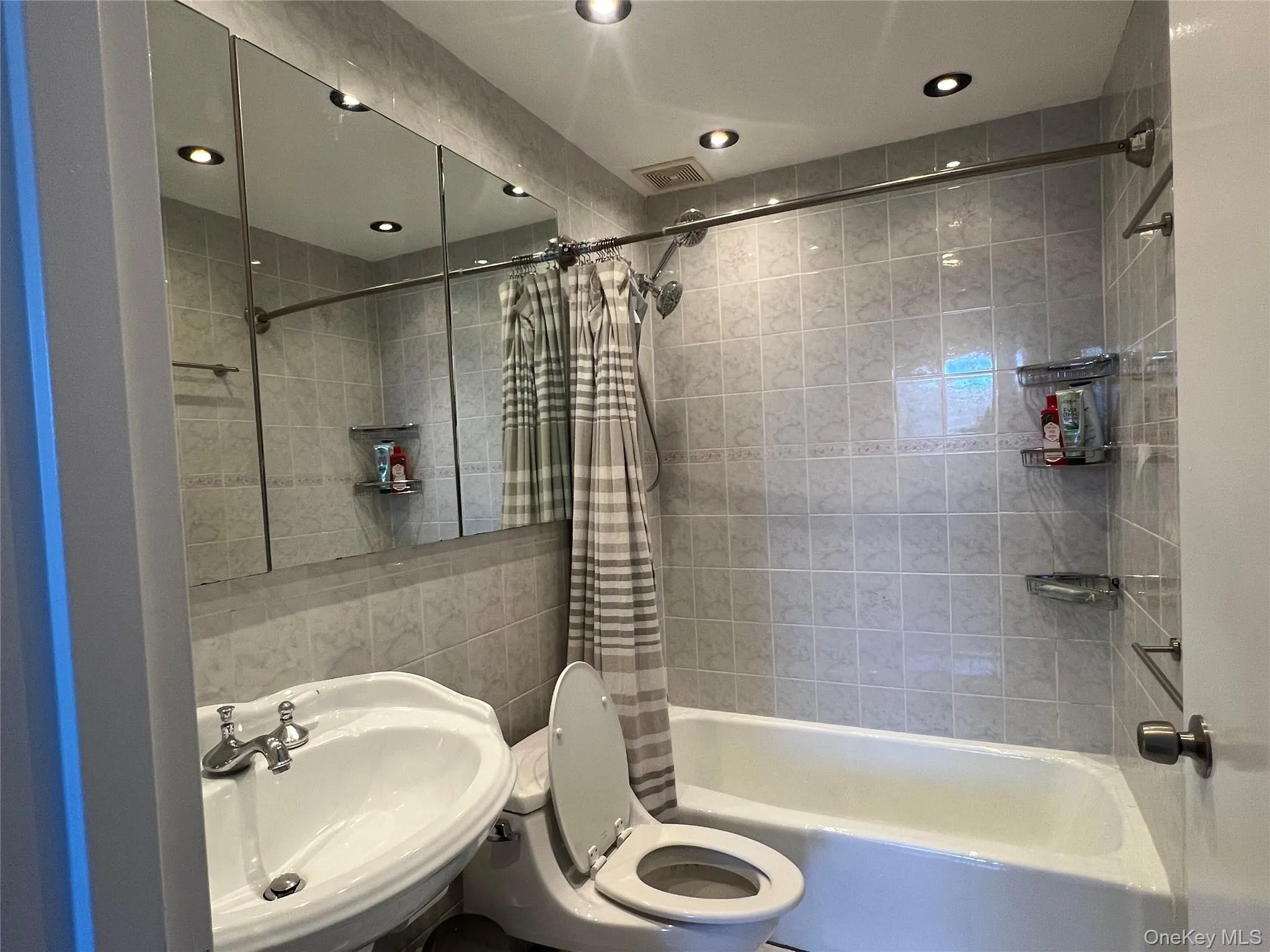 Bathroom featuring shower / bath combination with curtain, tile walls, and recessed lighting Bathroom featuring shower / bath combination with curtain, tile walls, and recessed lighting