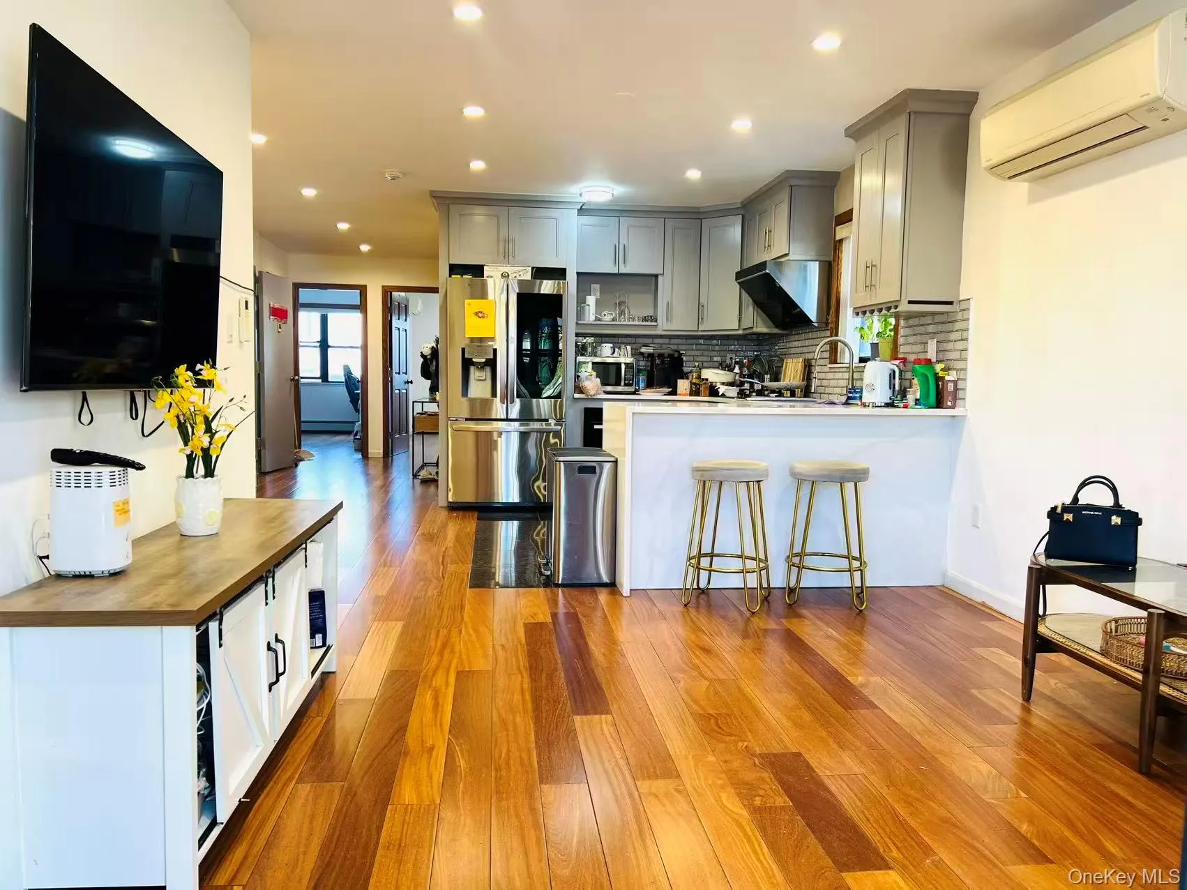 Kitchen featuring gray cabinets, stainless steel fridge with ice dispenser, a kitchen bar, light wood-type flooring, and a wall mounted AC Kitchen featuring gray cabinets, stainless steel fridge with ice dispenser, a kitchen bar, light wood-type flooring, and a wall mounted AC