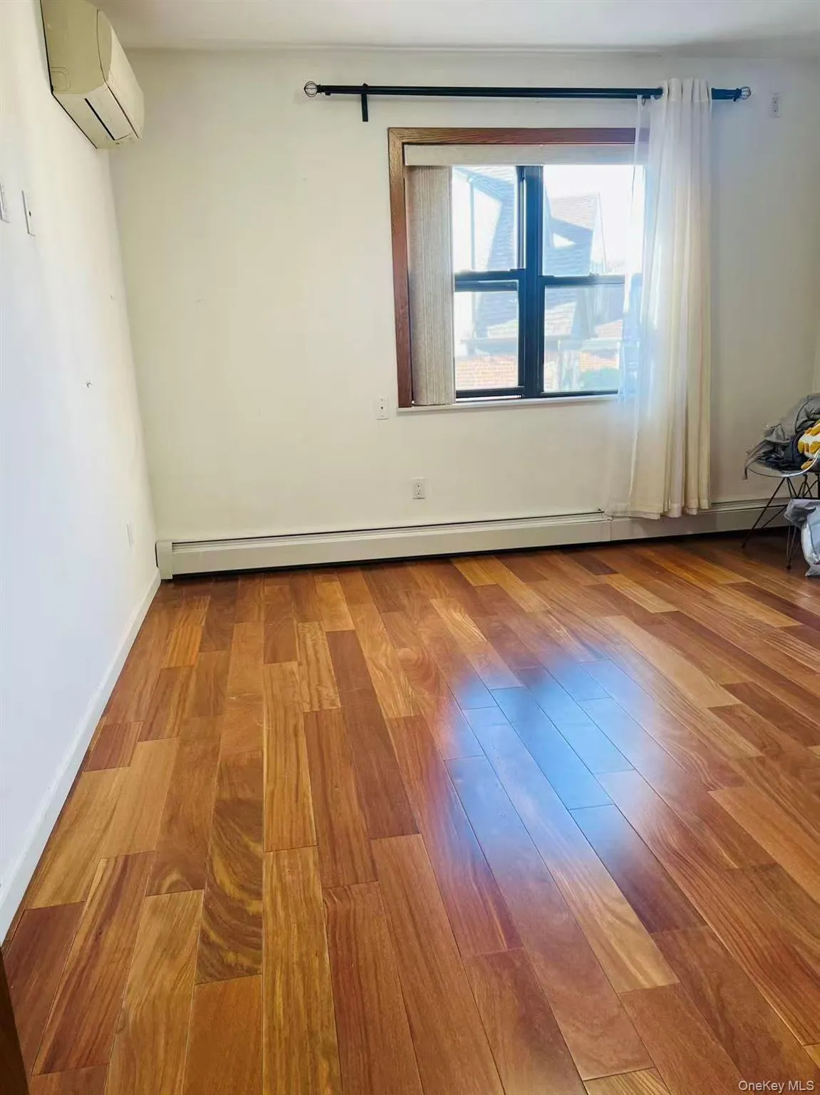 Empty room with wood finished floors, baseboard heating, and a wall unit AC Empty room with wood finished floors, baseboard heating, and a wall unit AC