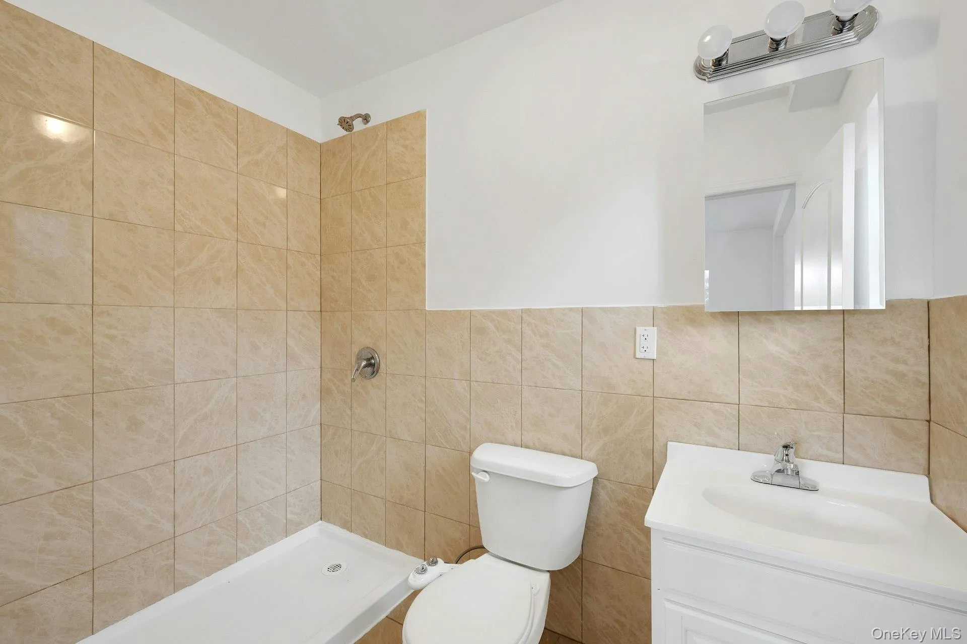 Bathroom featuring tiled shower, vanity, and tile walls Bathroom featuring tiled shower, vanity, and tile walls