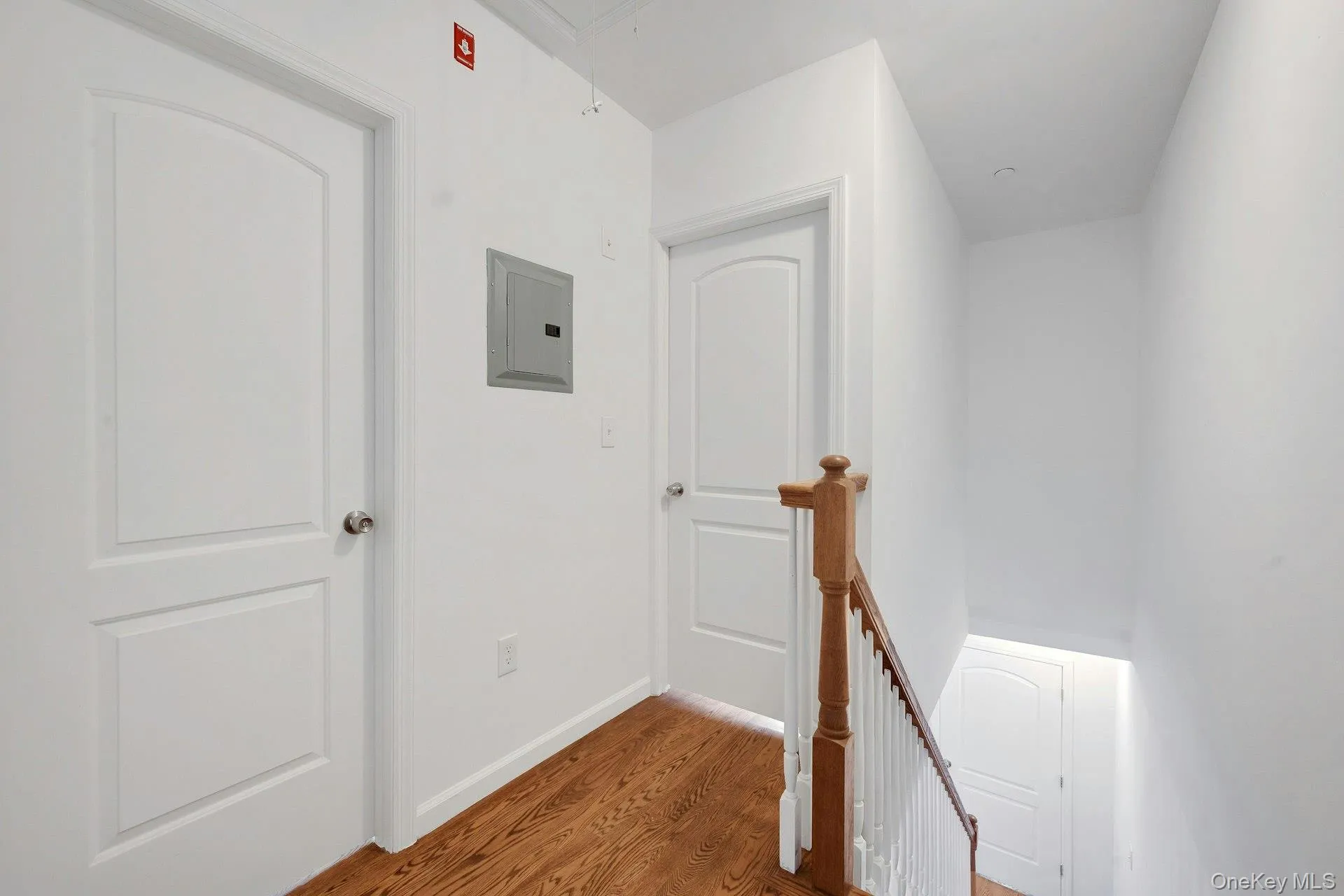 Hall featuring attic access, an upstairs landing, wood finished floors, and electric panel Hall featuring attic access, an upstairs landing, wood finished floors, and electric panel