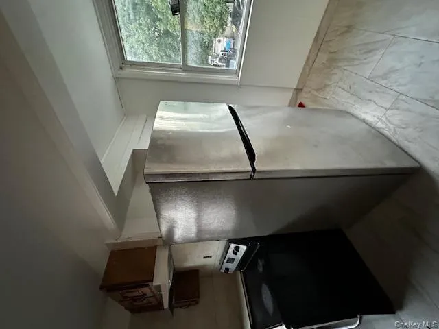 Kitchen featuring freestanding refrigerator, stove, light marble finish flooring, exhaust hood, and light countertops Kitchen featuring freestanding refrigerator, stove, light marble finish flooring, exhaust hood, and light countertops