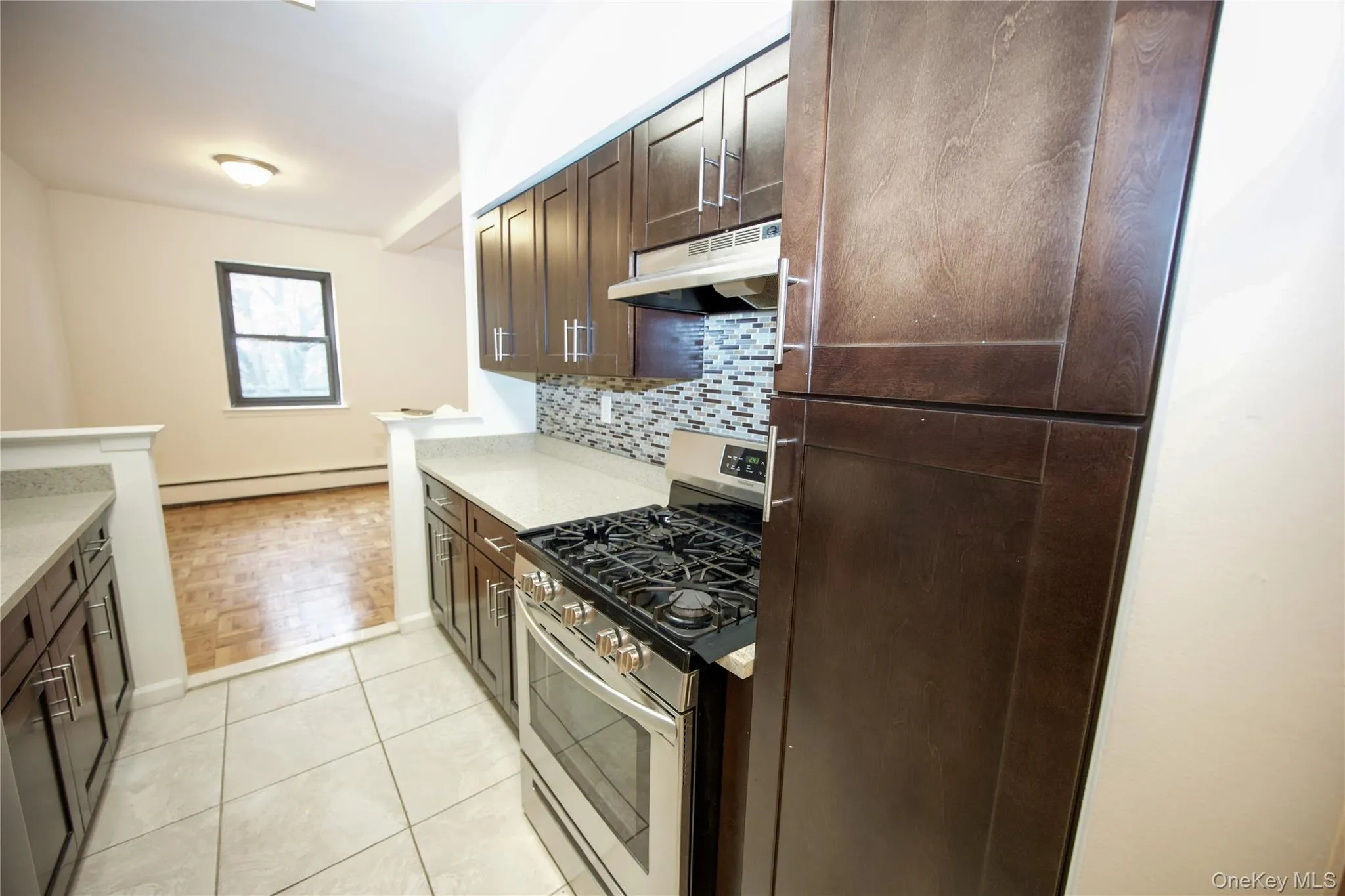 Kitchen with stainless steel range with gas stovetop, dark brown cabinetry, decorative backsplash, under cabinet range hood, and a baseboard heating unit Kitchen with stainless steel range with gas stovetop, dark brown cabinetry, decorative backsplash, under cabinet range hood, and a baseboard heating unit