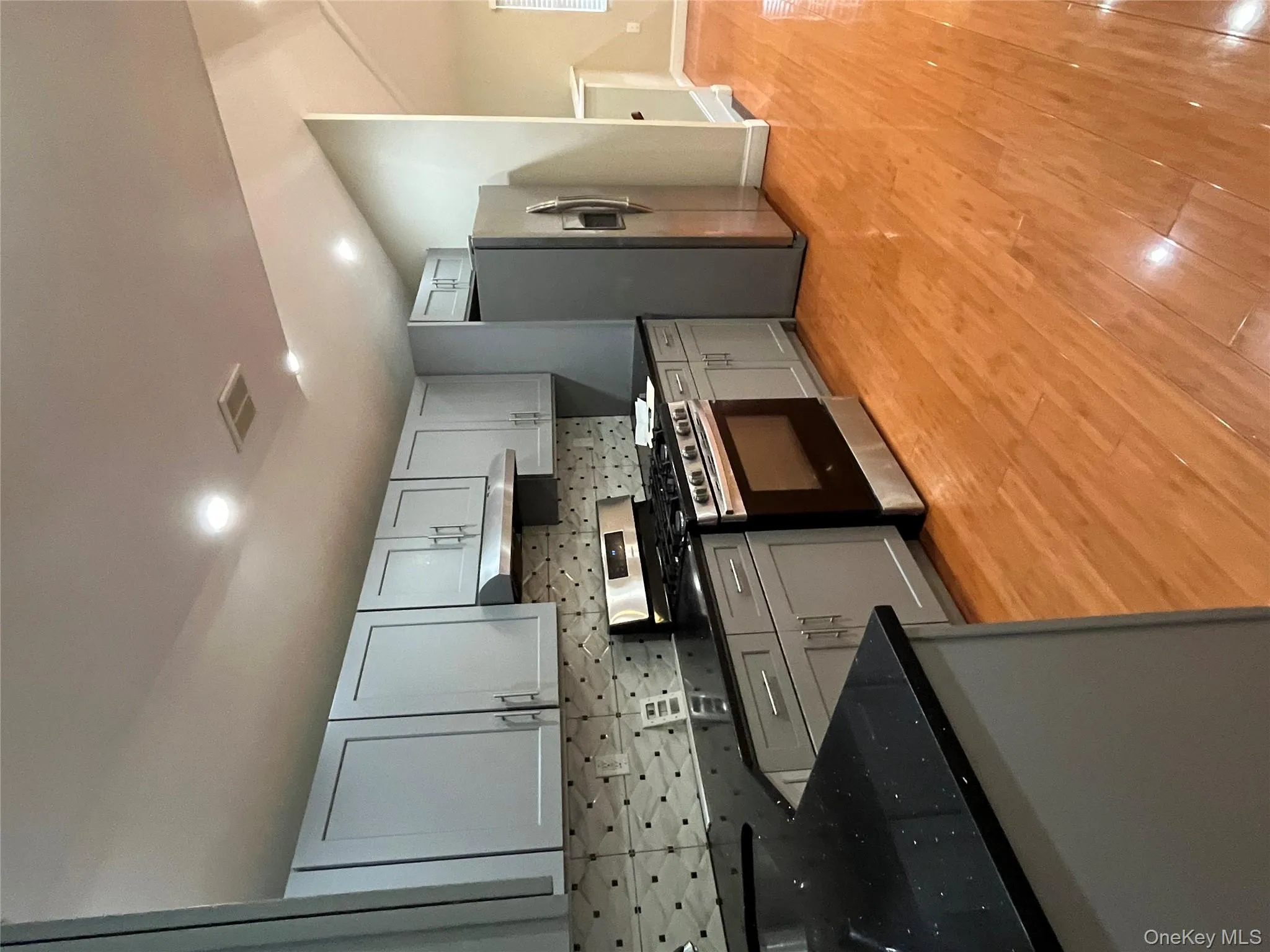 Kitchen with backsplash, stainless steel range oven, refrigerator, light wood finished floors, and dark stone counters Kitchen with backsplash, stainless steel range oven, refrigerator, light wood finished floors, and dark stone counters