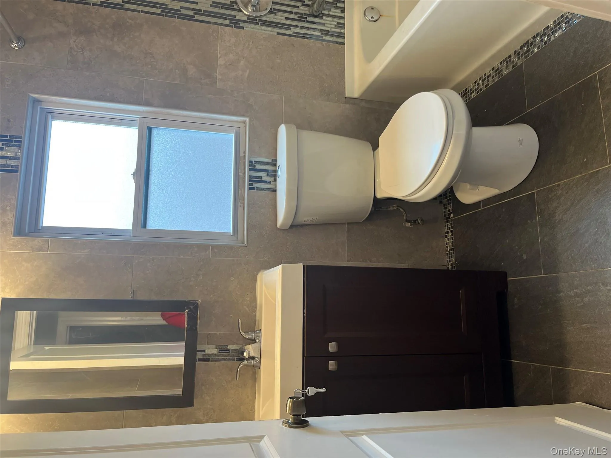 Full bath with tile walls, vanity, dark tile patterned floors, and shower / tub combination Full bath with tile walls, vanity, dark tile patterned floors, and shower / tub combination