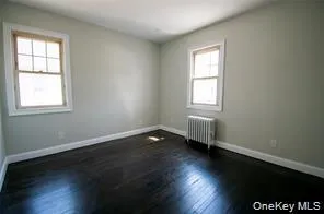 Spare room featuring dark wood-style flooring and radiator heating unit Spare room featuring dark wood-style flooring and radiator heating unit