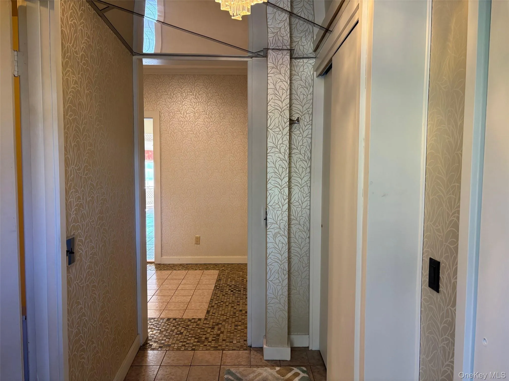 Hallway featuring wallpapered walls, tile patterned floors, and a chandelier Hallway featuring wallpapered walls, tile patterned floors, and a chandelier
