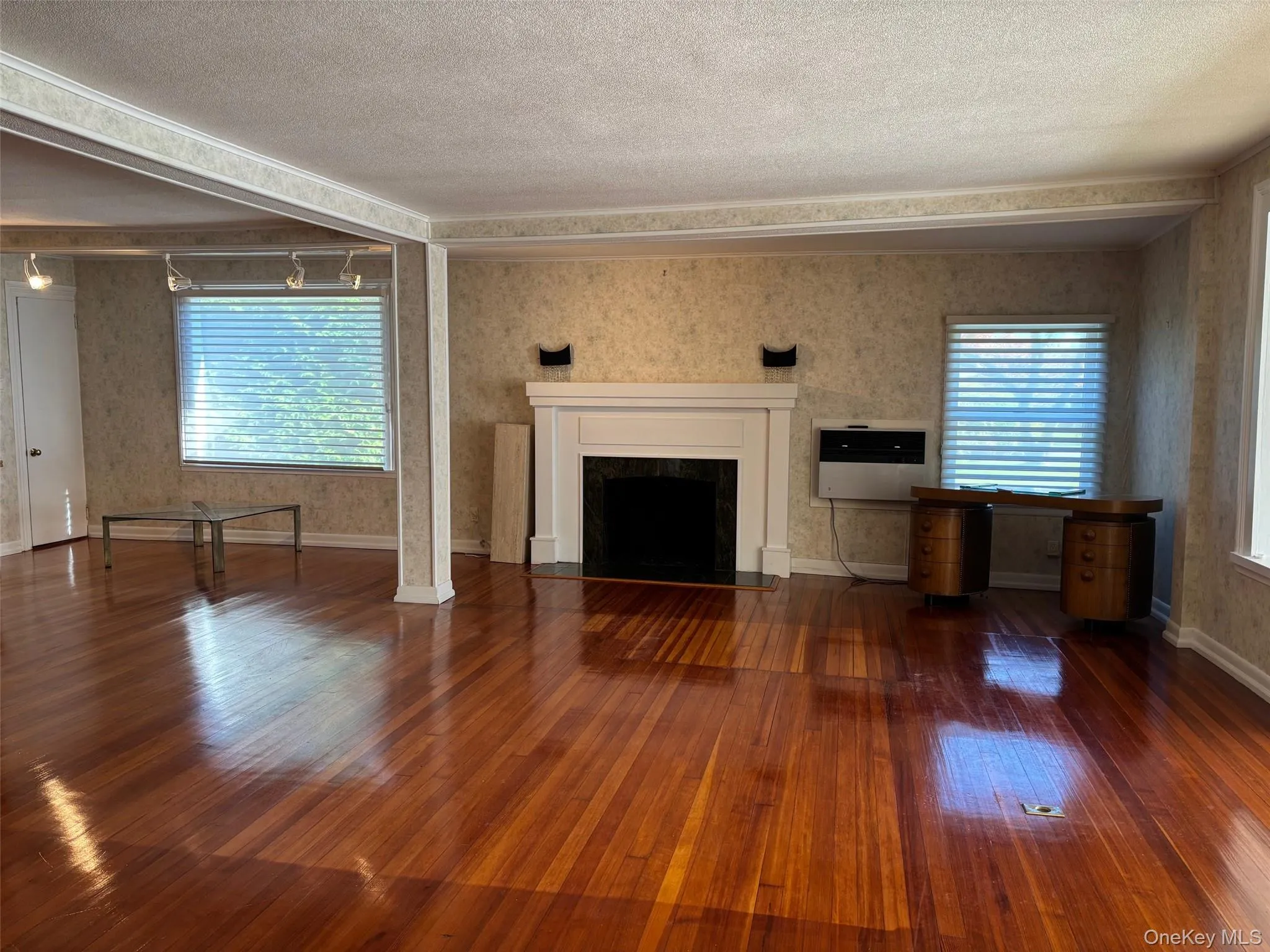 Unfurnished living room with a fireplace, dark wood-style flooring, wallpapered walls, a textured ceiling, and heating unit Unfurnished living room with a fireplace, dark wood-style flooring, wallpapered walls, a textured ceiling, and heating unit