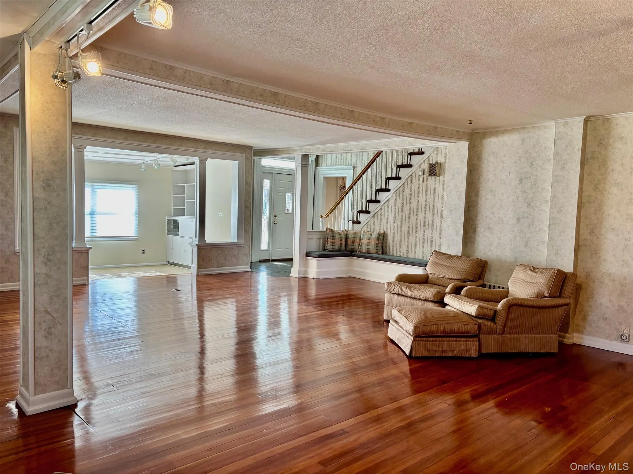 Living area featuring wood-type flooring, a textured ceiling, wallpapered walls, stairs, and ornate columns Living area featuring wood-type flooring, a textured ceiling, wallpapered walls, stairs, and ornate columns