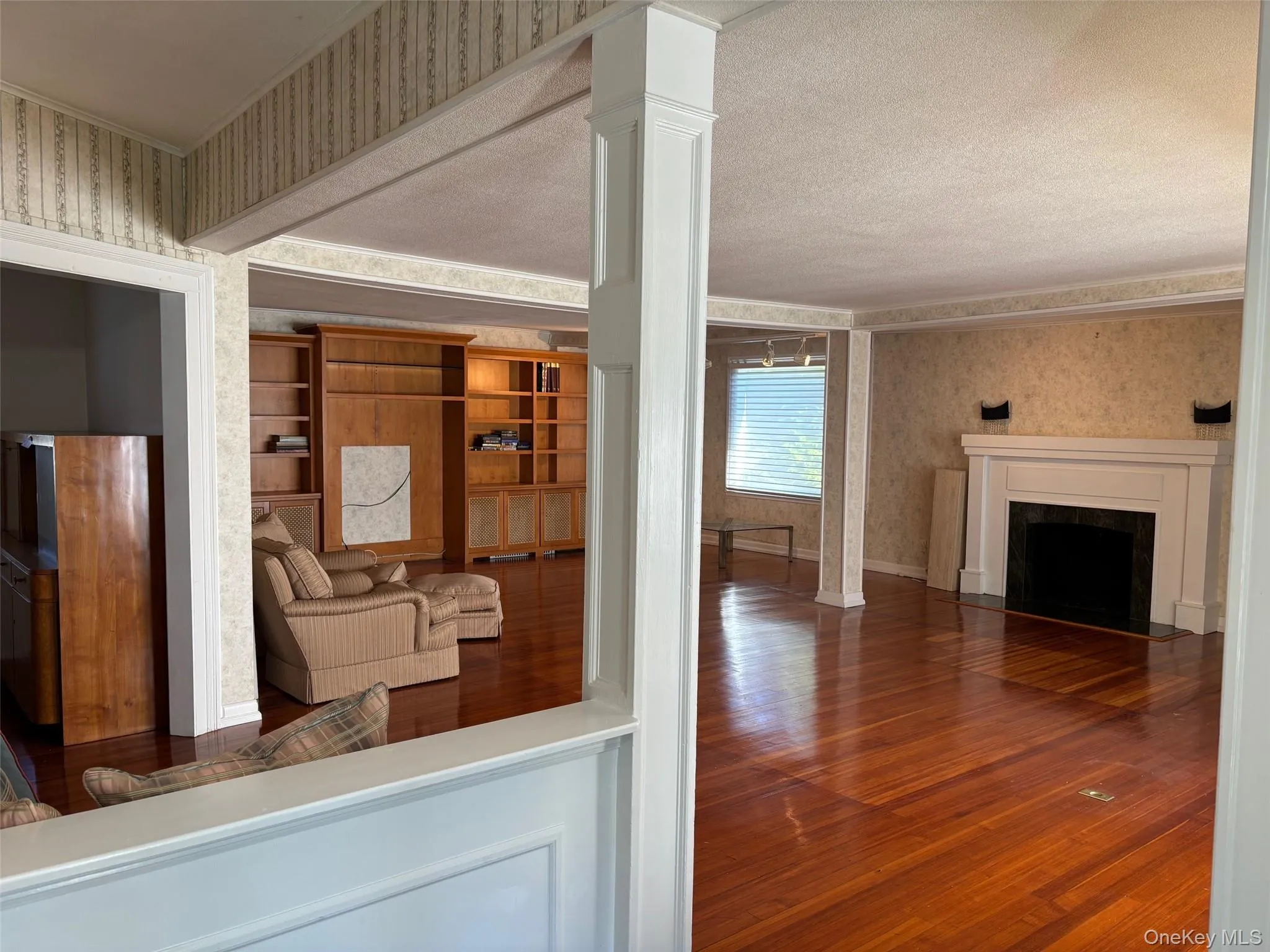 Unfurnished living room with wallpapered walls, wood-type flooring, and a fireplace with flush hearth Unfurnished living room with wallpapered walls, wood-type flooring, and a fireplace with flush hearth