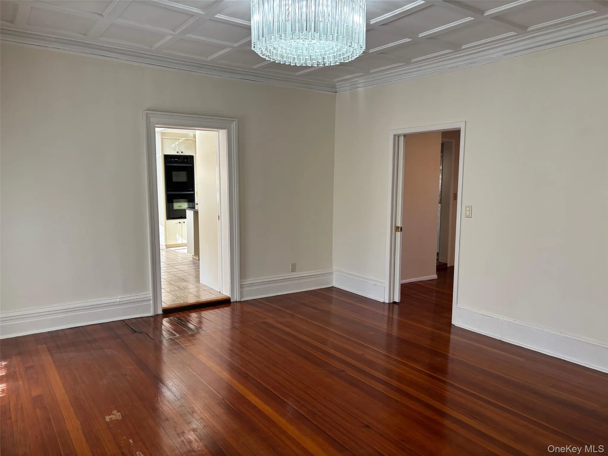 Unfurnished room with dark wood-type flooring, a chandelier, and an ornate ceiling Unfurnished room with dark wood-type flooring, a chandelier, and an ornate ceiling