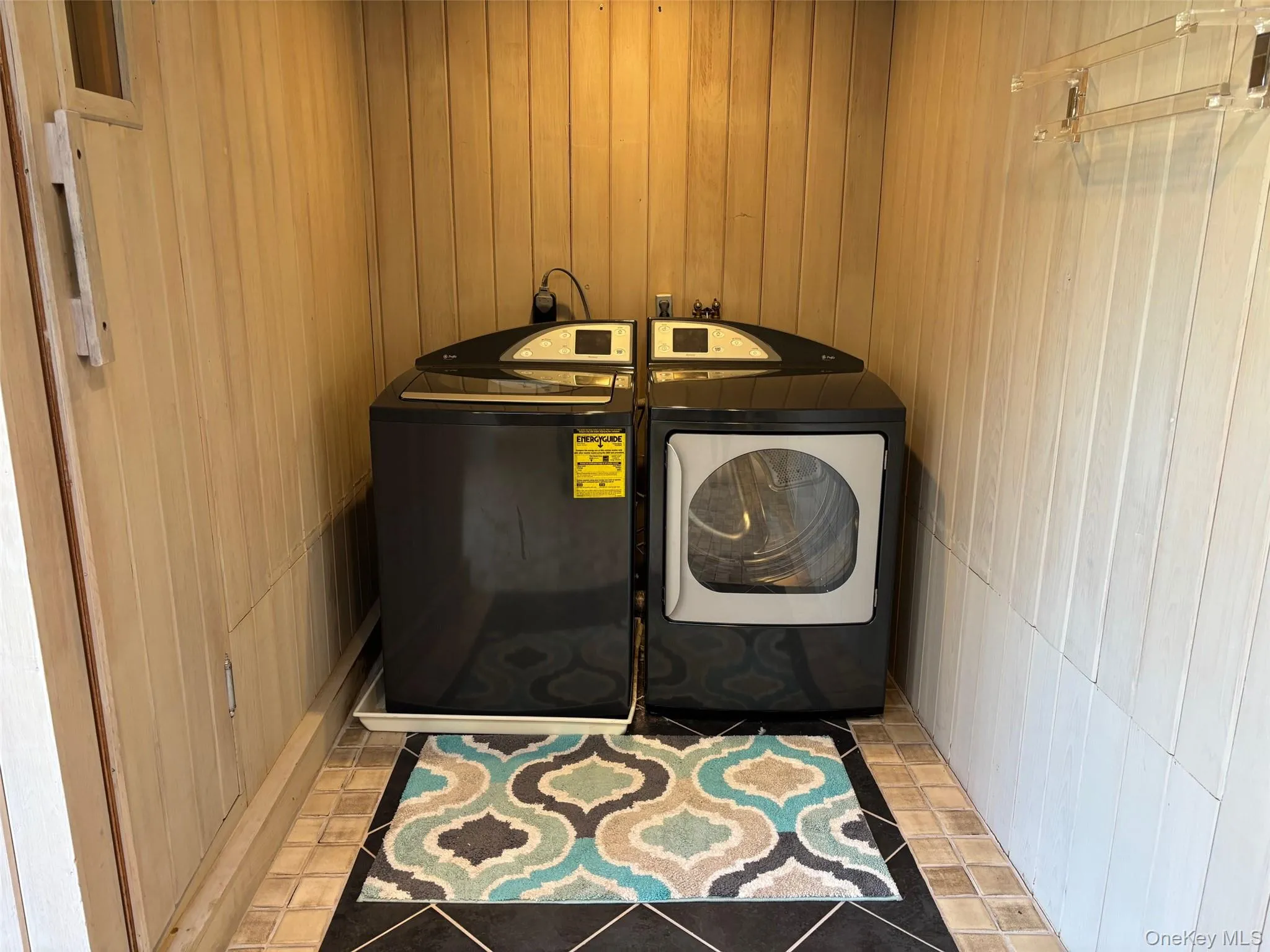 Washroom with washer and clothes dryer, wooden walls, and light tile patterned floors Washroom with washer and clothes dryer, wooden walls, and light tile patterned floors