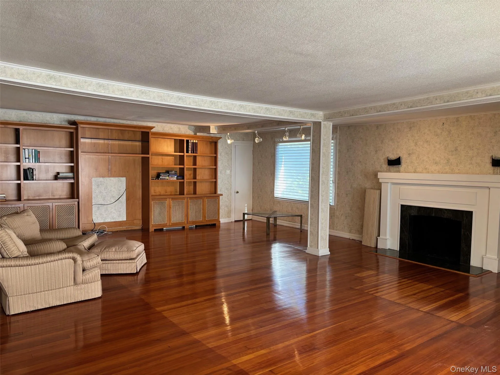 Unfurnished living room featuring dark wood-style flooring, a fireplace, wallpapered walls, and a textured ceiling Unfurnished living room featuring dark wood-style flooring, a fireplace, wallpapered walls, and a textured ceiling