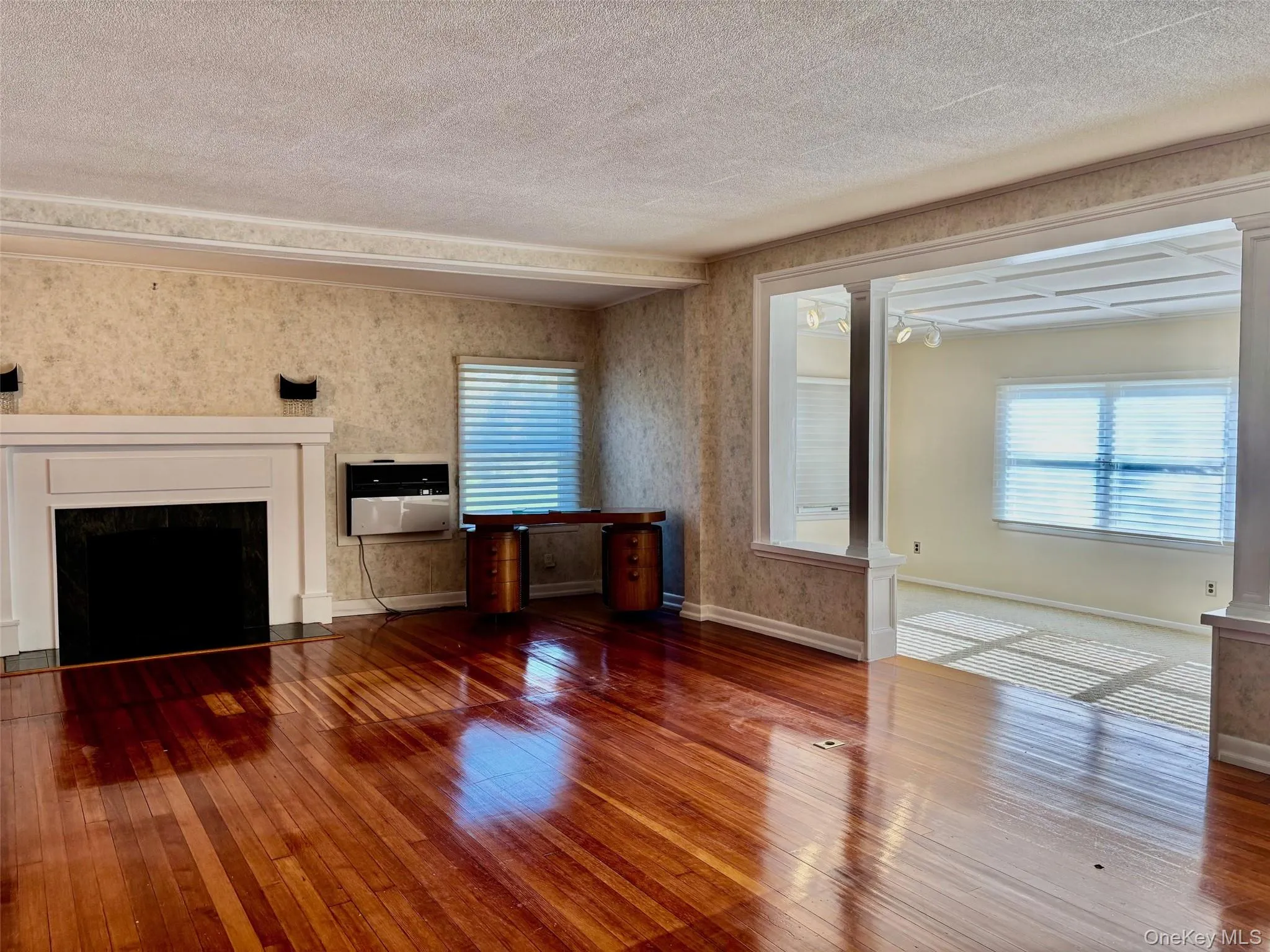 Unfurnished living room featuring a fireplace with flush hearth, hardwood / wood-style flooring, wallpapered walls, heating unit, and a textured ceiling Unfurnished living room featuring a fireplace with flush hearth, hardwood / wood-style flooring, wallpapered walls, heating unit, and a textured ceiling