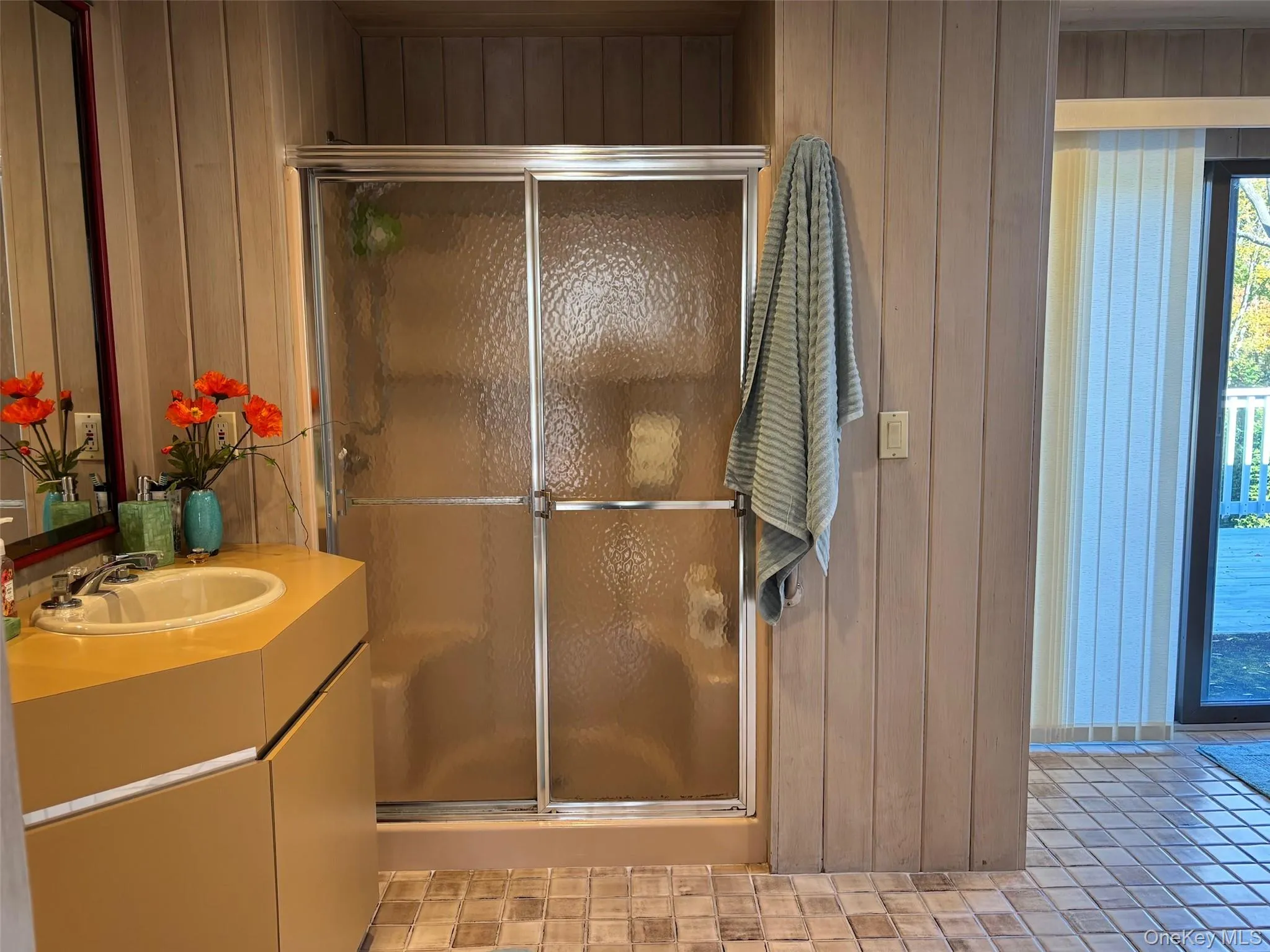 Bathroom featuring a shower stall, vanity, wooden walls, and light tile patterned floors Bathroom featuring a shower stall, vanity, wooden walls, and light tile patterned floors