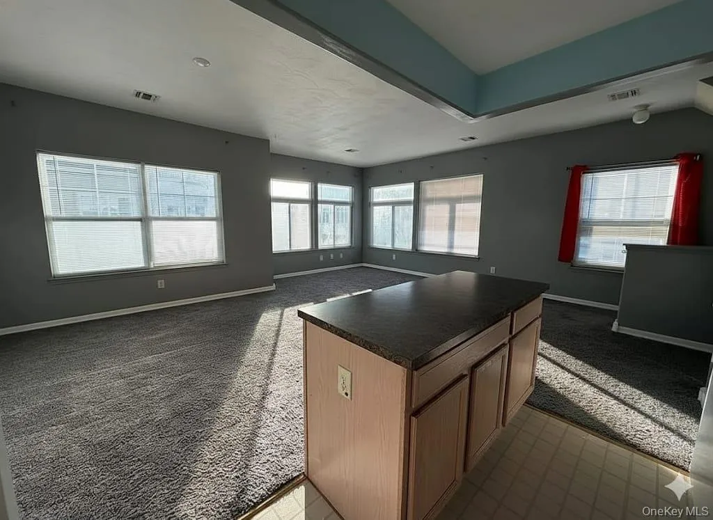 Kitchen featuring light colored carpet, open floor plan, and dark countertops Kitchen featuring light colored carpet, open floor plan, and dark countertops