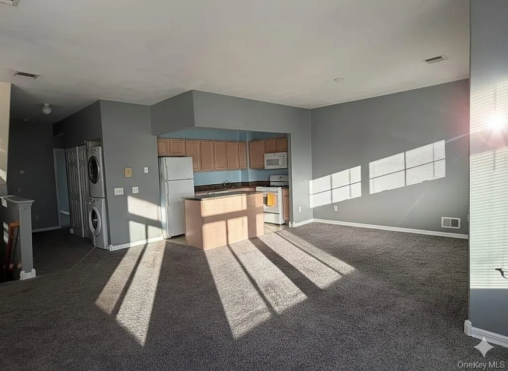 Kitchen featuring open floor plan, stacked washer / dryer, white appliances, a kitchen island, and light colored carpet Kitchen featuring open floor plan, stacked washer / dryer, white appliances, a kitchen island, and light colored carpet