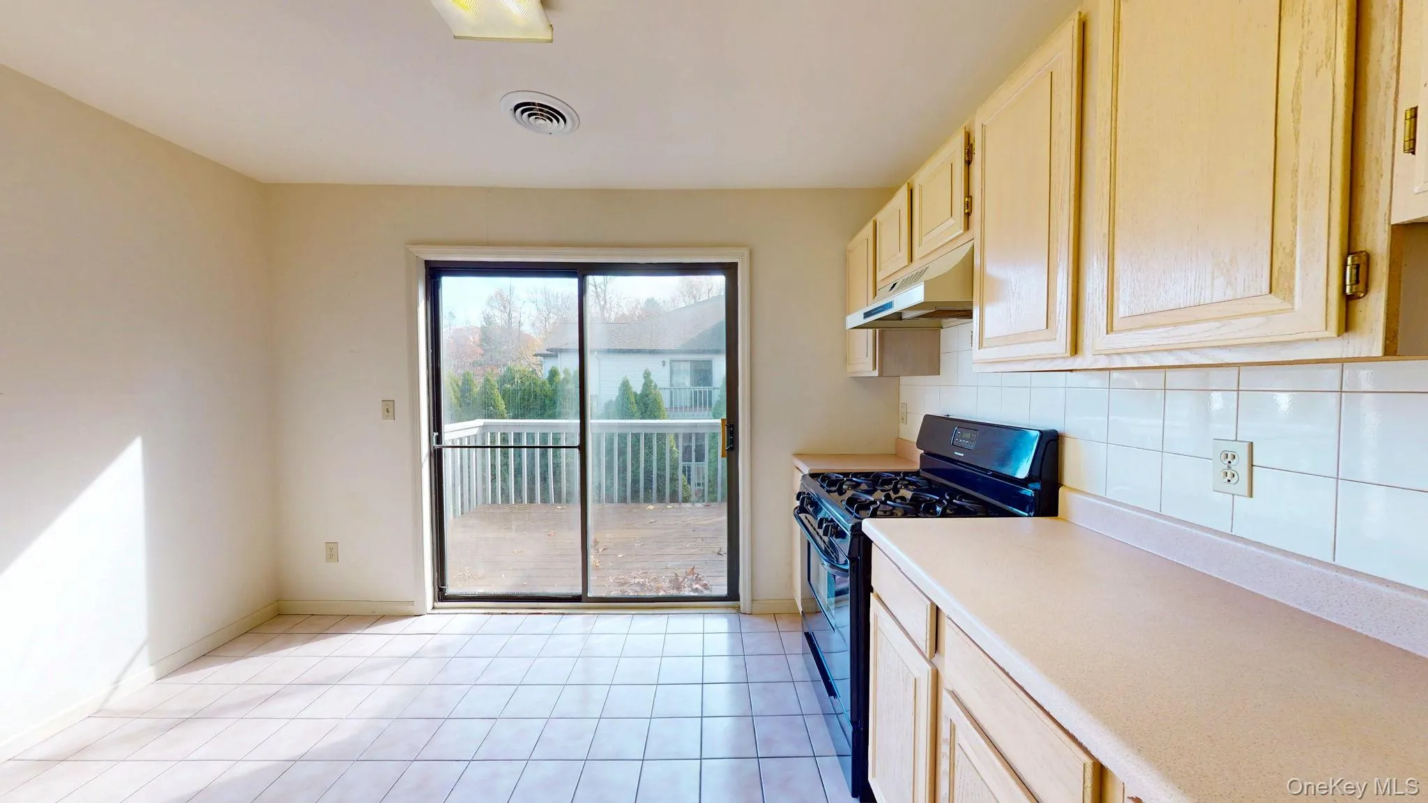 Kitchen featuring black range with gas stovetop, light countertops, light brown cabinets, decorative backsplash, and light tile patterned flooring Kitchen featuring black range with gas stovetop, light countertops, light brown cabinets, decorative backsplash, and light tile patterned flooring