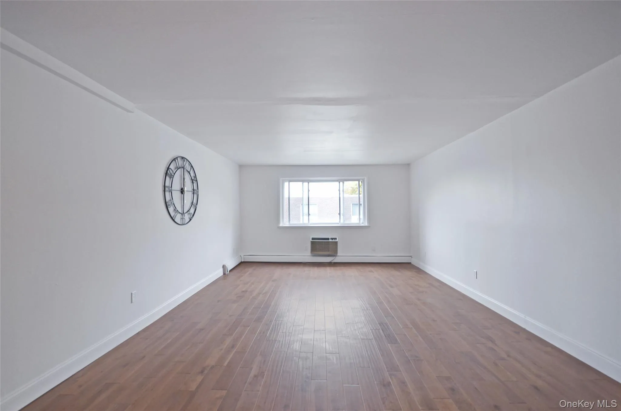 Spare room featuring wood finished floors, an AC wall unit, and a baseboard heating unit Spare room featuring wood finished floors, an AC wall unit, and a baseboard heating unit