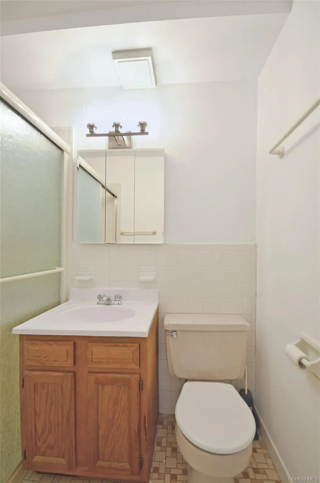Full bathroom featuring vanity, tile walls, a shower with shower door, light tile patterned floors, and a wainscoted wall Full bathroom featuring vanity, tile walls, a shower with shower door, light tile patterned floors, and a wainscoted wall