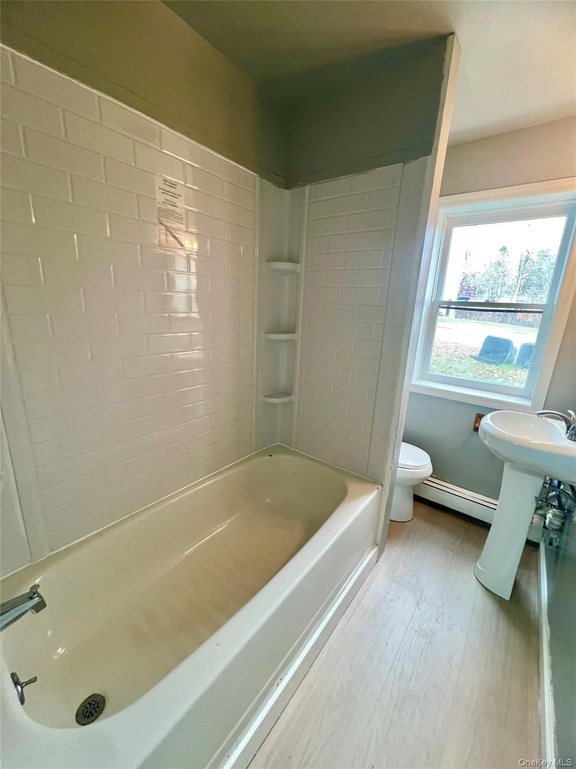 Bathroom with washtub / shower combination, light wood-style floors, and baseboard heating Bathroom with washtub / shower combination, light wood-style floors, and baseboard heating
