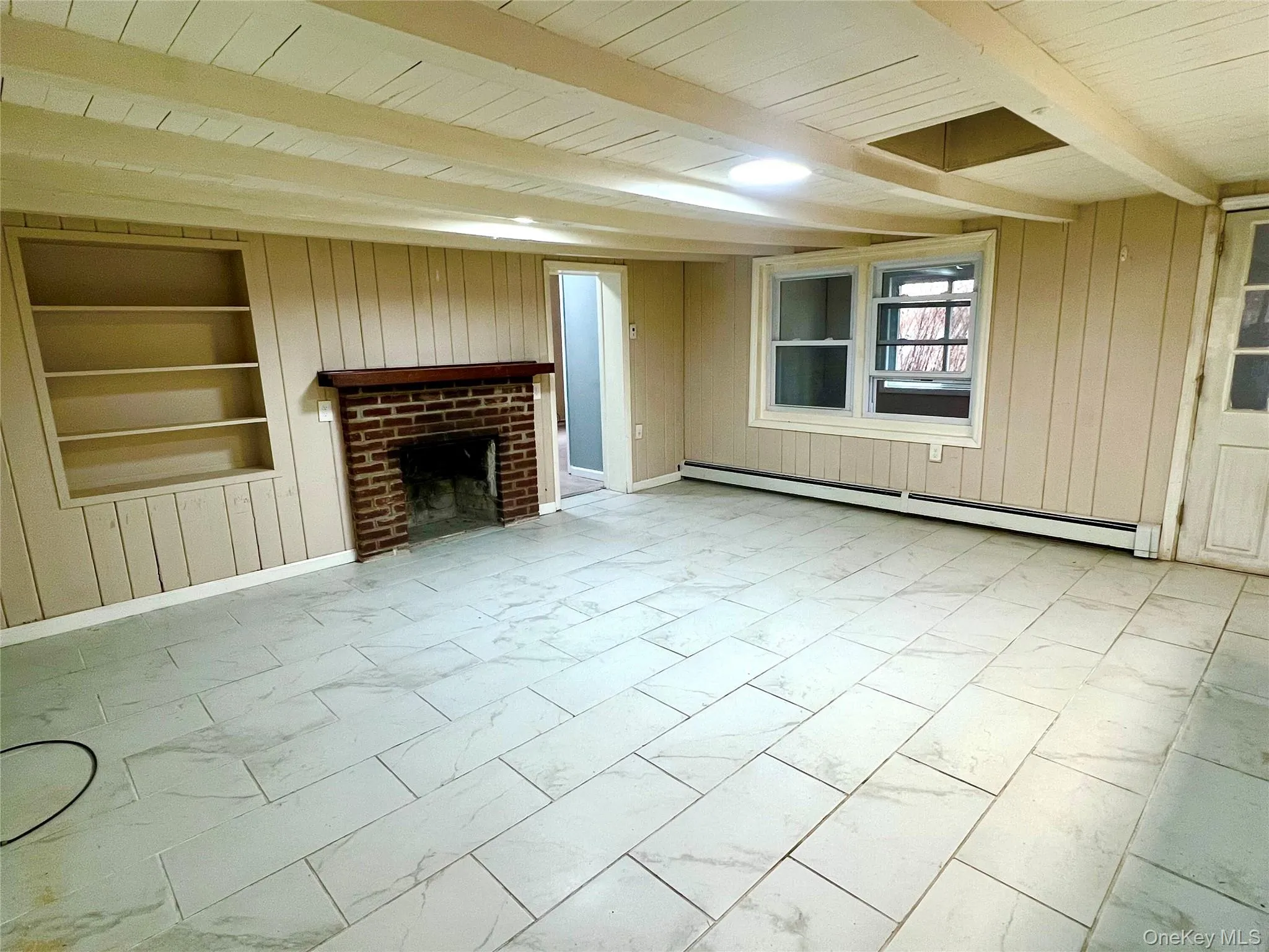 Unfurnished living room featuring built in features, light marble finish flooring, a fireplace, a baseboard heating unit, and wooden walls Unfurnished living room featuring built in features, light marble finish flooring, a fireplace, a baseboard heating unit, and wooden walls