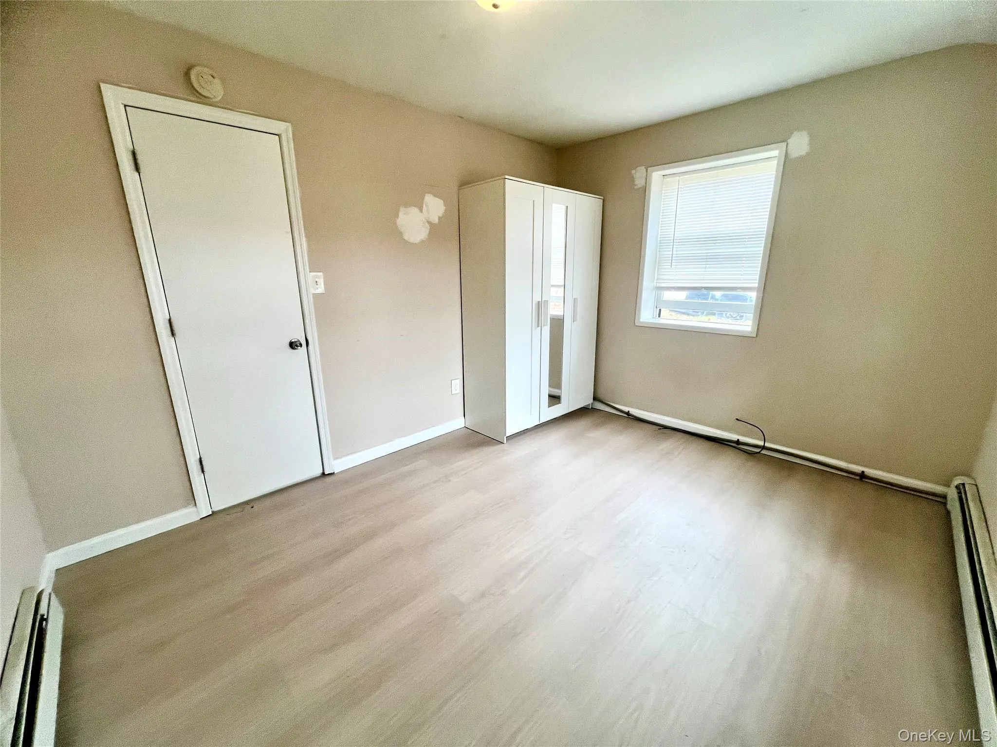 Unfurnished bedroom featuring baseboard heating, a baseboard heating unit, and light wood-style floors Unfurnished bedroom featuring baseboard heating, a baseboard heating unit, and light wood-style floors