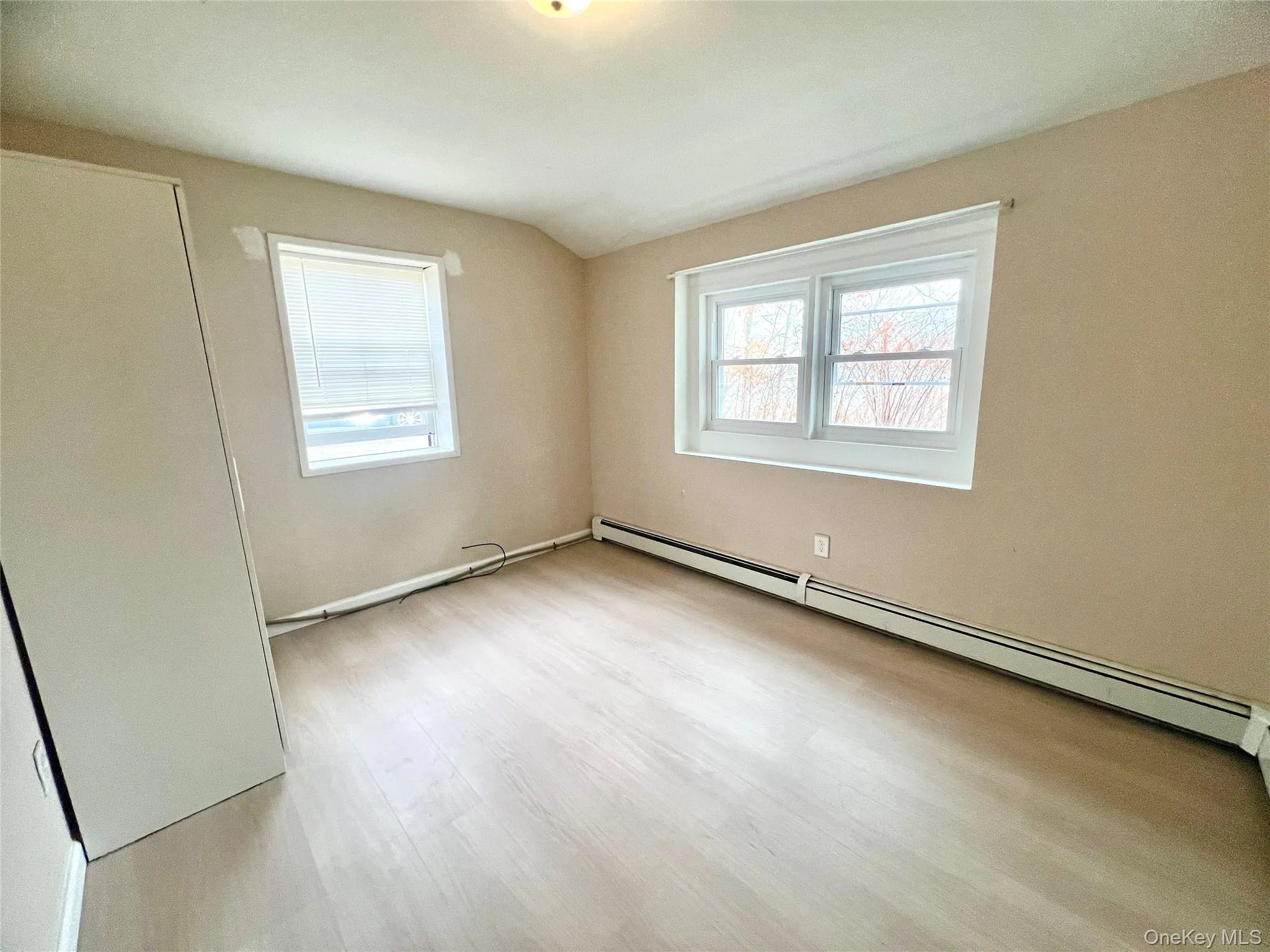 Unfurnished bedroom with a baseboard radiator, light wood-style floors, and vaulted ceiling Unfurnished bedroom with a baseboard radiator, light wood-style floors, and vaulted ceiling