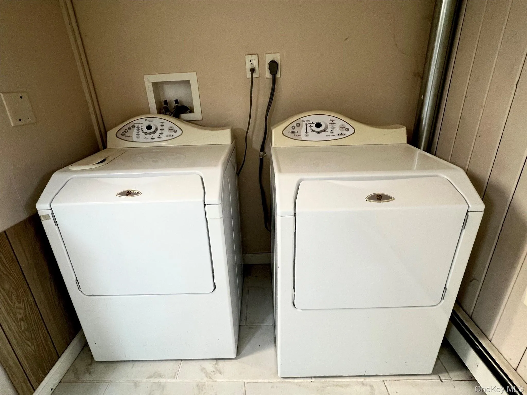 Laundry area featuring wood walls, washing machine and clothes dryer, light tile patterned floors, and a baseboard heating unit Laundry area featuring wood walls, washing machine and clothes dryer, light tile patterned floors, and a baseboard heating unit