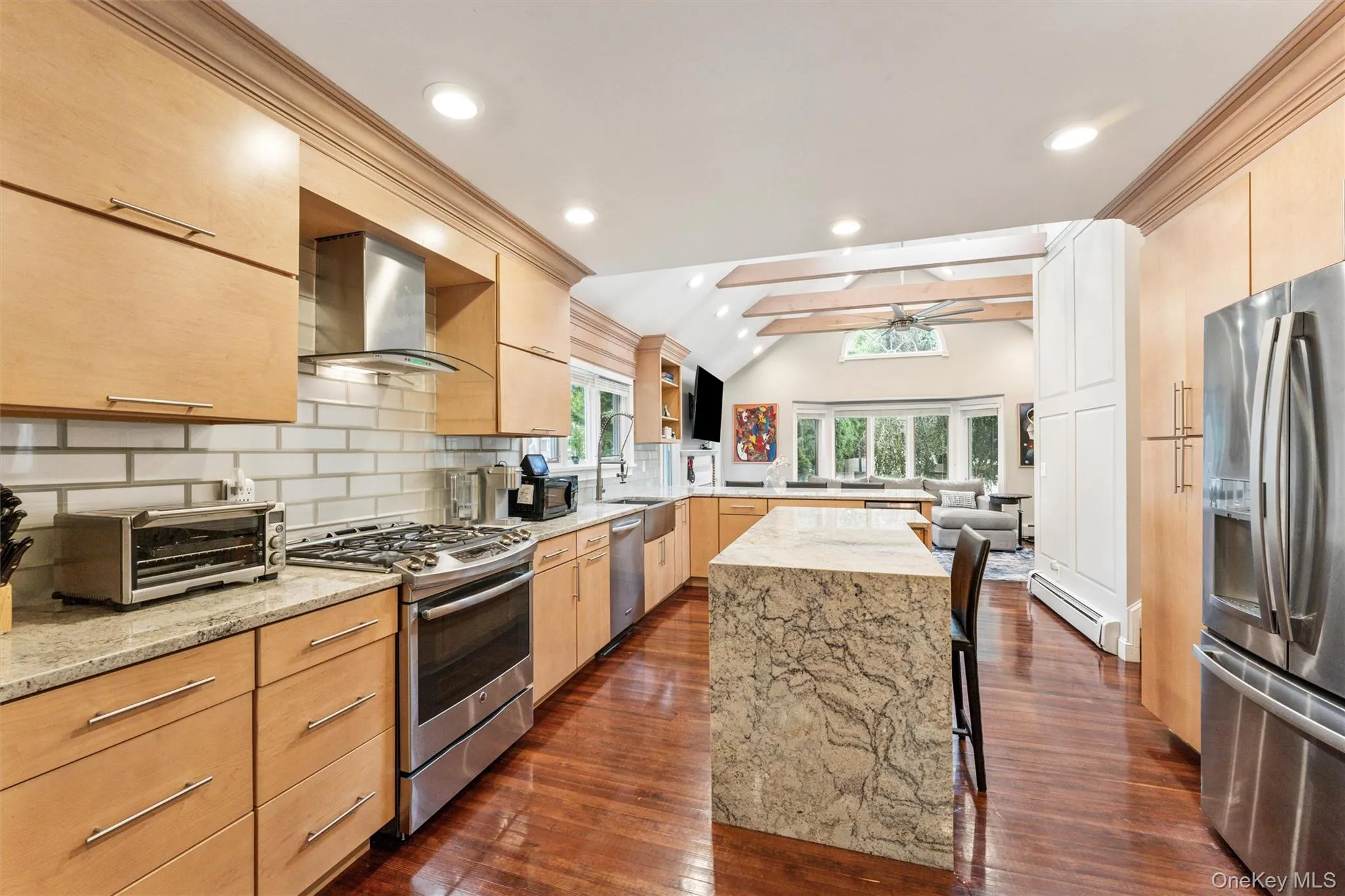Kitchen with light brown cabinets, light stone counters, stainless steel appliances, tasteful backsplash, and wall chimney exhaust hood Kitchen with light brown cabinets, light stone counters, stainless steel appliances, tasteful backsplash, and wall chimney exhaust hood