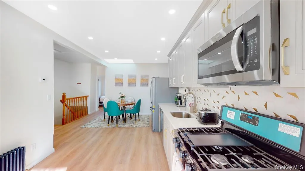 Kitchen featuring stainless steel appliances, light wood finished floors, white cabinets, radiator, and backsplash Kitchen featuring stainless steel appliances, light wood finished floors, white cabinets, radiator, and backsplash
