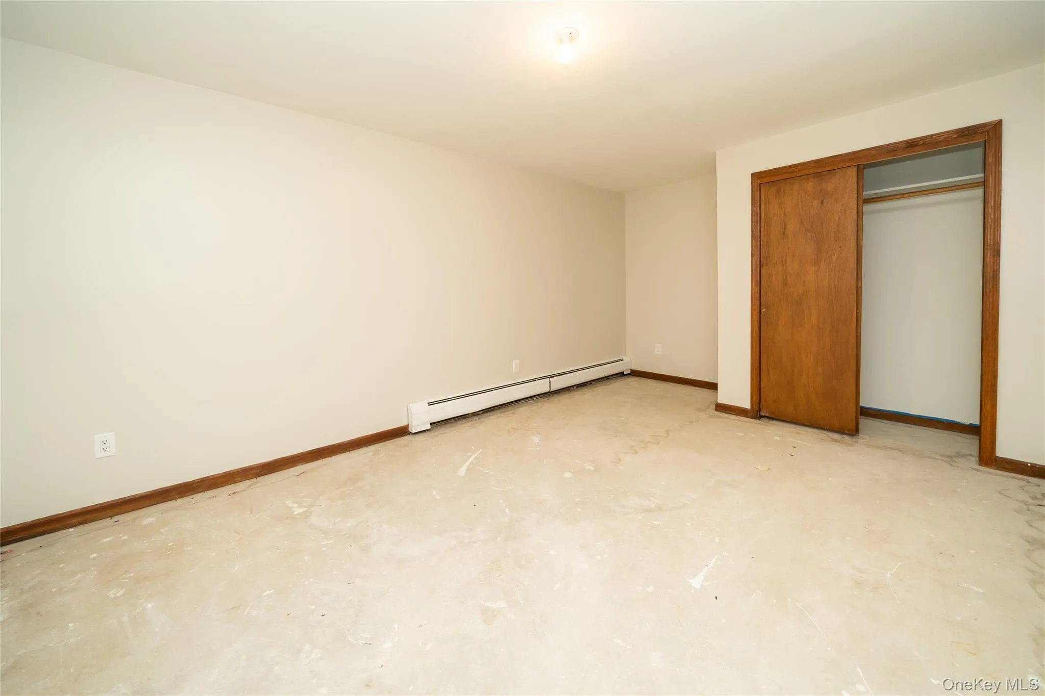 Unfurnished bedroom with baseboard heating, unfinished concrete floors, and a closet Unfurnished bedroom with baseboard heating, unfinished concrete floors, and a closet