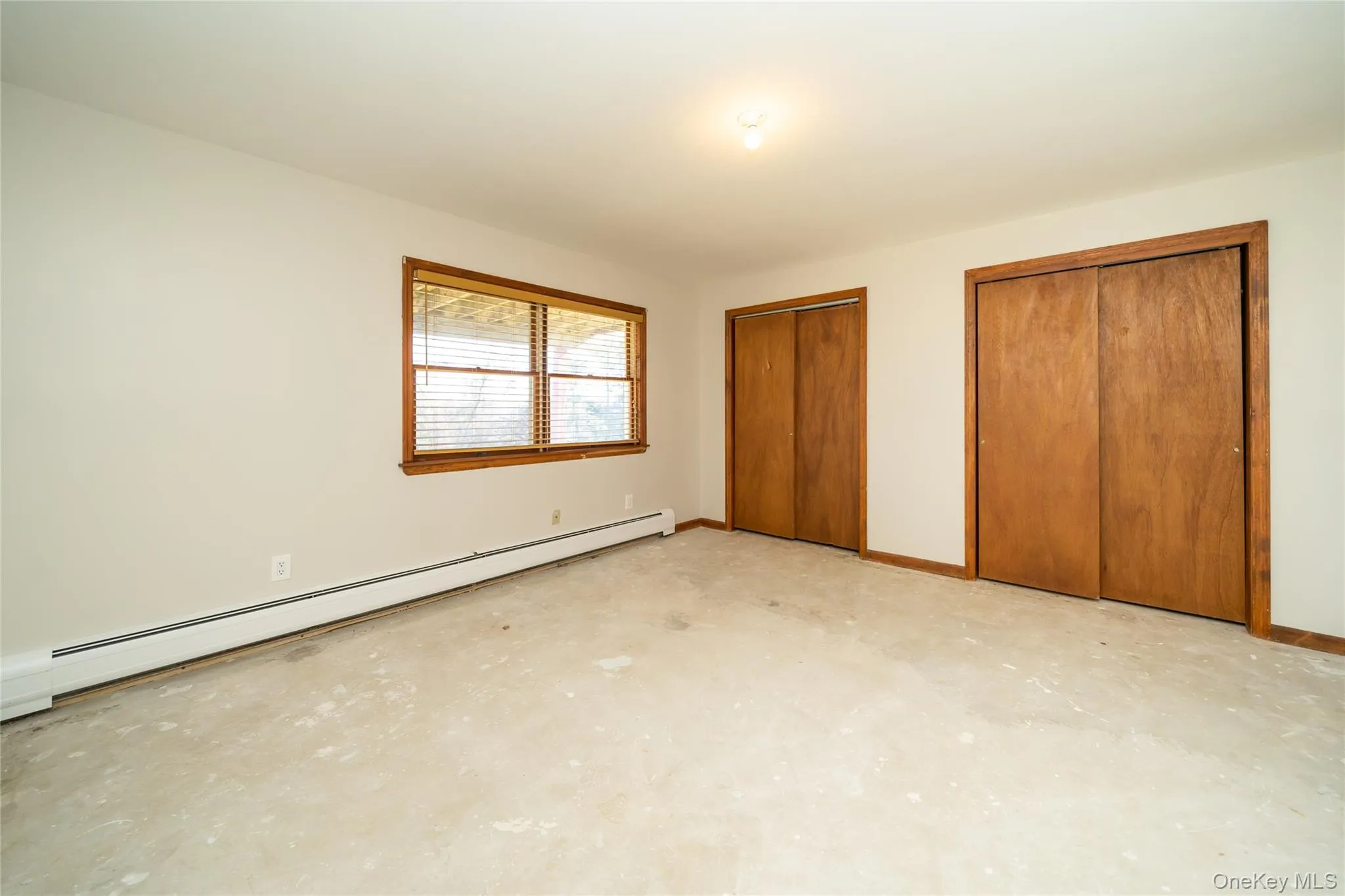 Unfurnished bedroom featuring a baseboard heating unit, multiple closets, and concrete flooring Unfurnished bedroom featuring a baseboard heating unit, multiple closets, and concrete flooring