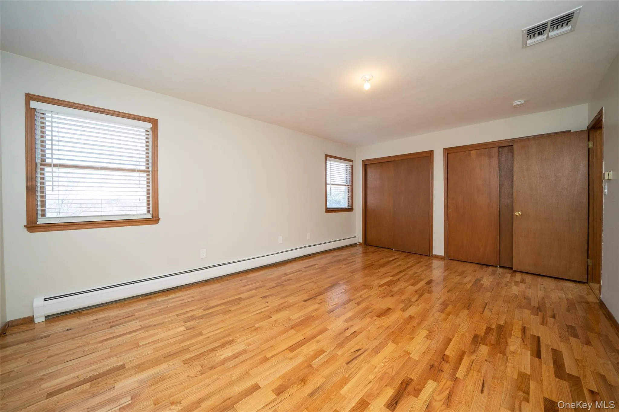 Unfurnished bedroom with a baseboard radiator, multiple closets, and light wood-style flooring Unfurnished bedroom with a baseboard radiator, multiple closets, and light wood-style flooring