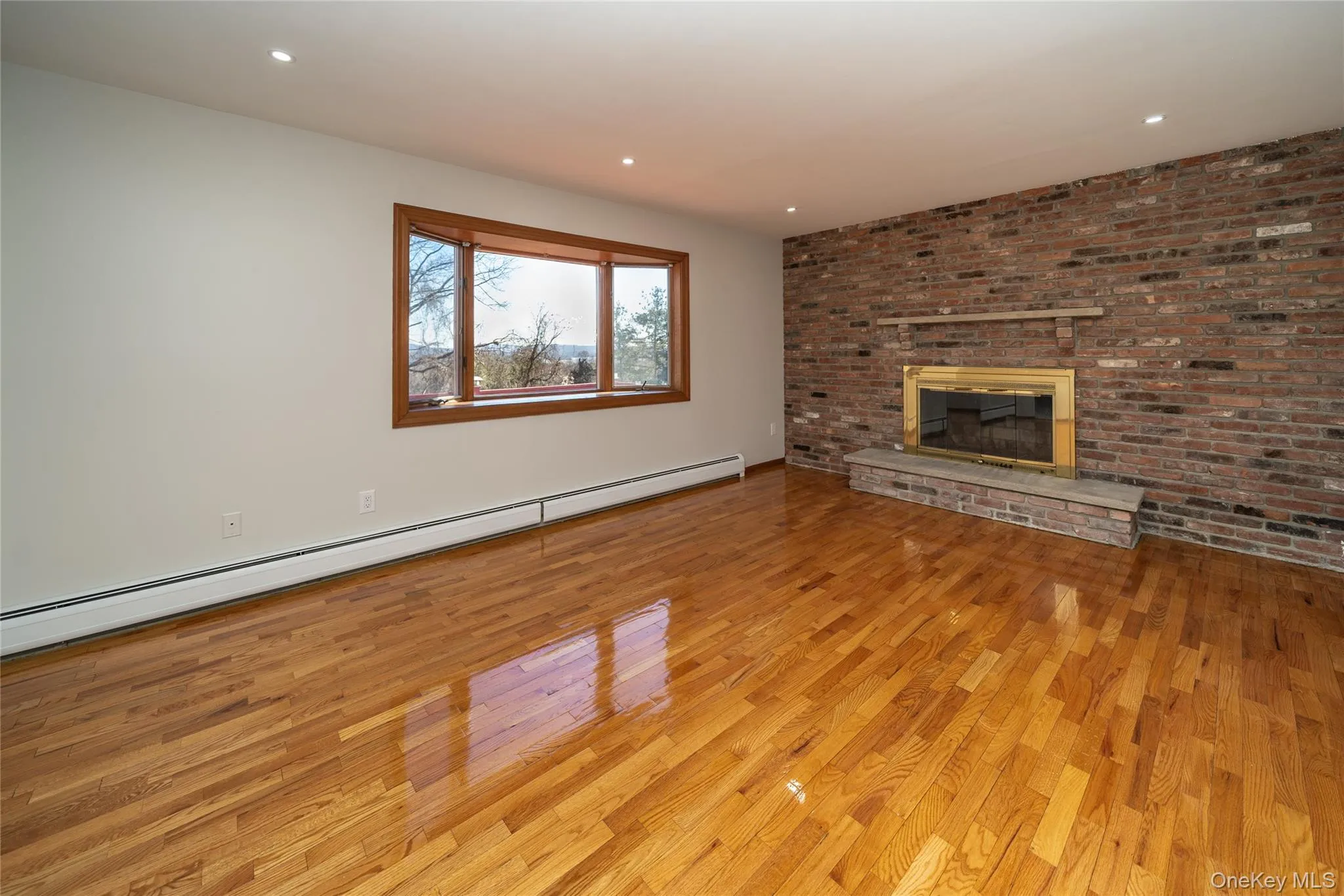 Unfurnished living room with a baseboard radiator, brick wall, light wood-style floors, a fireplace, and recessed lighting Unfurnished living room with a baseboard radiator, brick wall, light wood-style floors, a fireplace, and recessed lighting