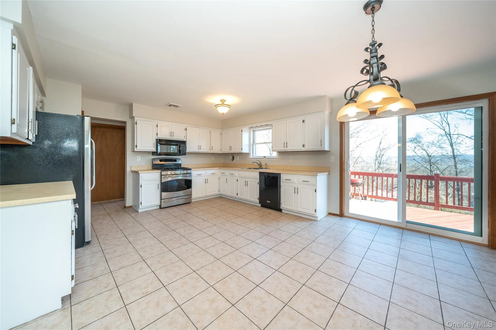 Kitchen featuring light countertops, black appliances, light tile patterned floors, and decorative light fixtures Kitchen featuring light countertops, black appliances, light tile patterned floors, and decorative light fixtures