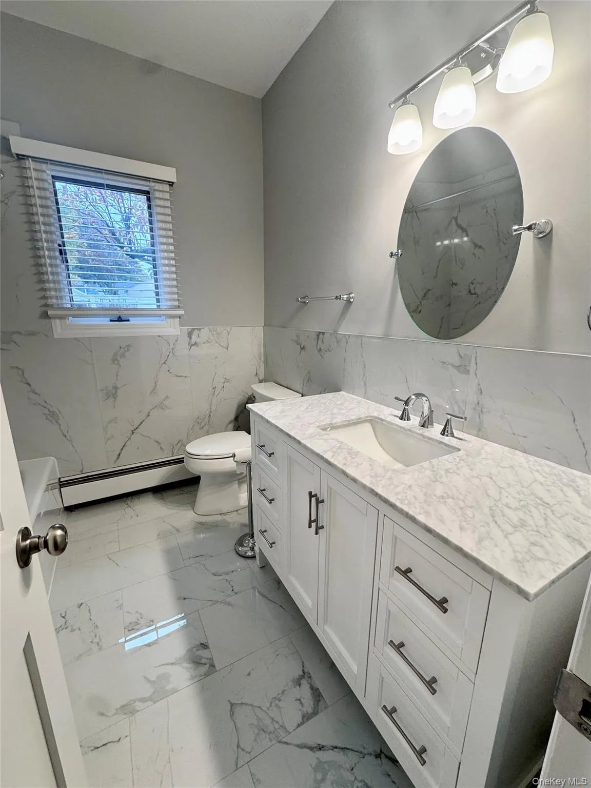 Full bathroom with vanity, tile walls, light marble finish floors, wainscoting, and baseboard heating Full bathroom with vanity, tile walls, light marble finish floors, wainscoting, and baseboard heating