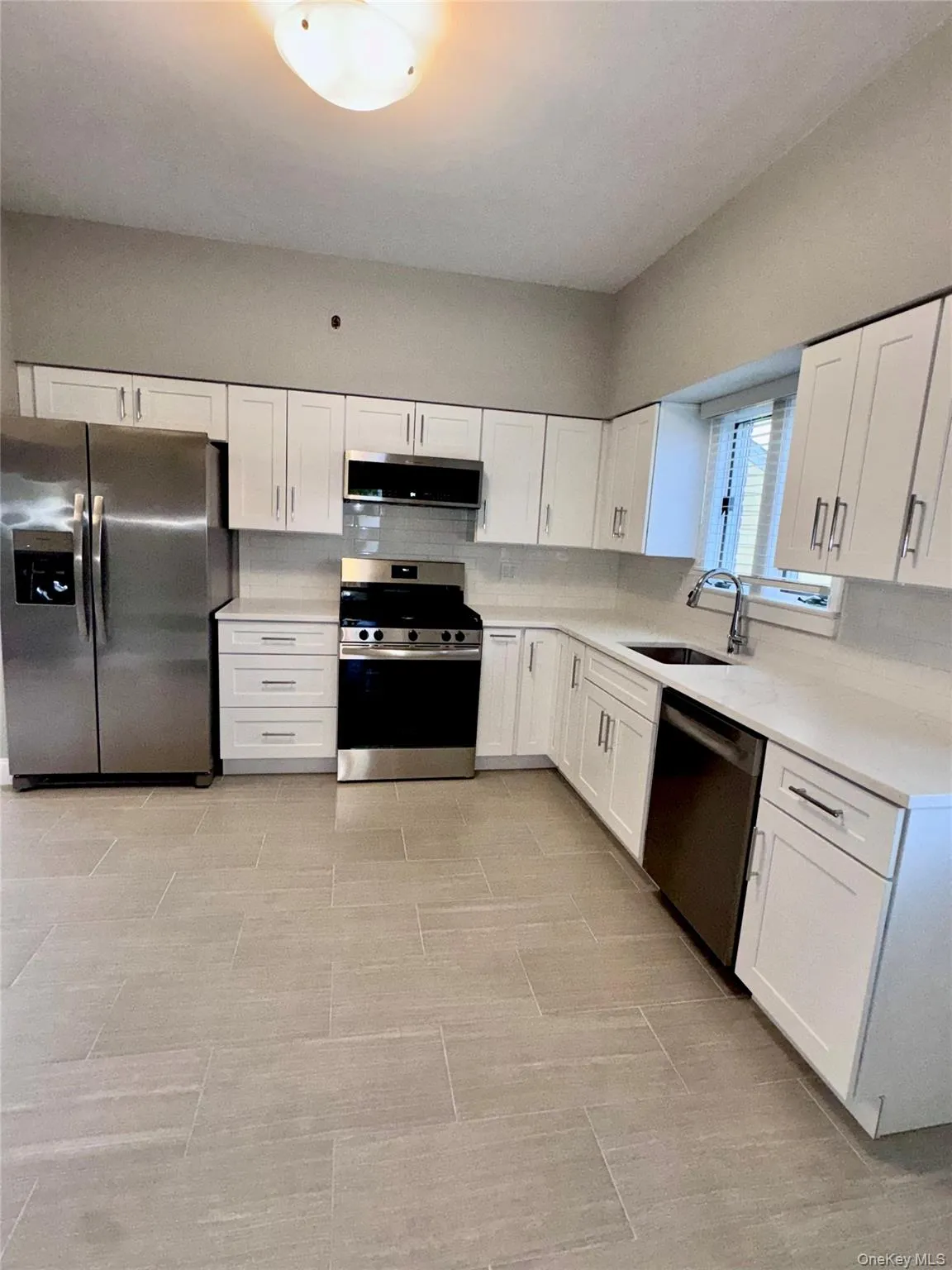 Kitchen featuring appliances with stainless steel finishes, white cabinets, backsplash, and light stone counters Kitchen featuring appliances with stainless steel finishes, white cabinets, backsplash, and light stone counters