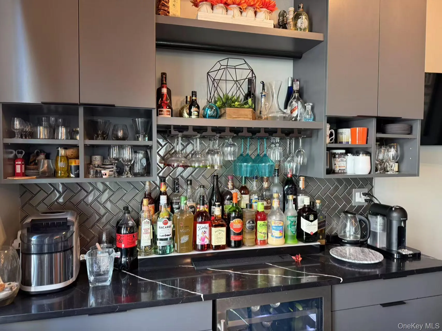 Indoor dry bar featuring open shelves, backsplash, dark stone counters, wine cooler, and gray cabinets Indoor dry bar featuring open shelves, backsplash, dark stone counters, wine cooler, and gray cabinets