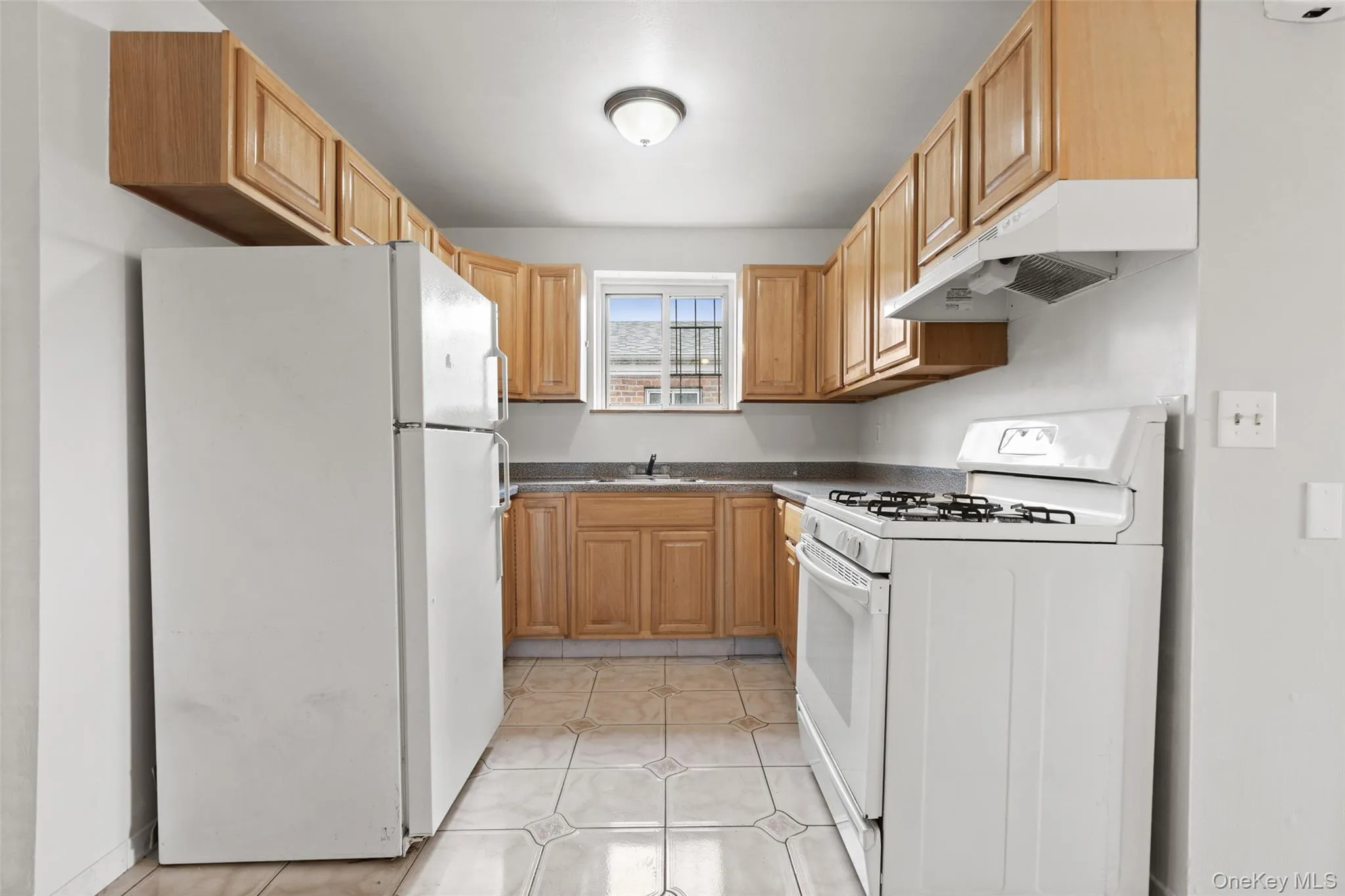 Kitchen with white appliances, light tile patterned floors, under cabinet range hood, and light brown cabinets Kitchen with white appliances, light tile patterned floors, under cabinet range hood, and light brown cabinets