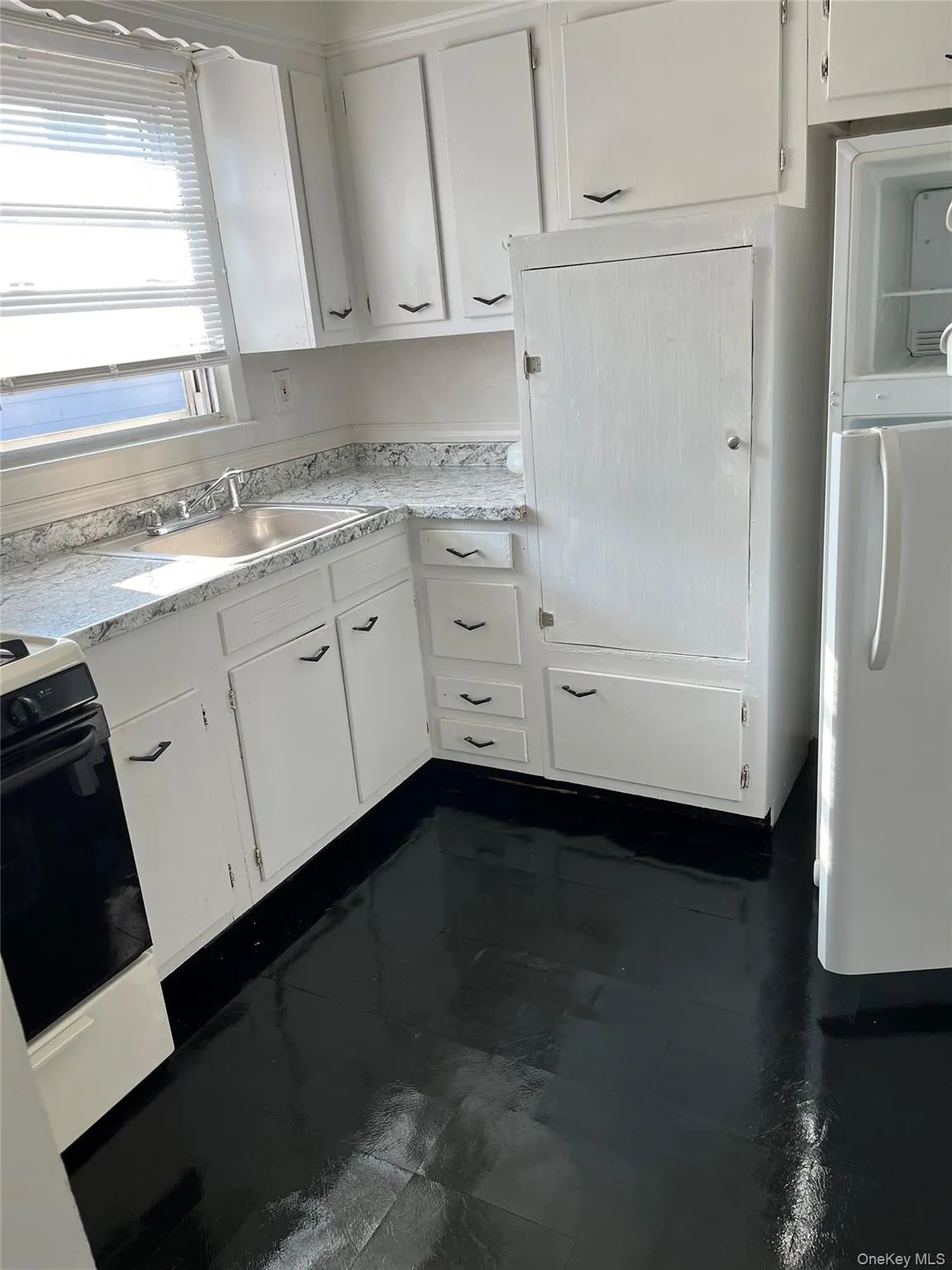 Kitchen featuring white cabinets, black stove, light countertops, and freestanding refrigerator Kitchen featuring white cabinets, black stove, light countertops, and freestanding refrigerator