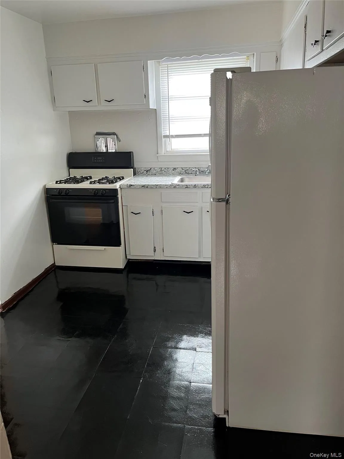 Kitchen with freestanding refrigerator, gas stove, white cabinets, and light countertops Kitchen with freestanding refrigerator, gas stove, white cabinets, and light countertops