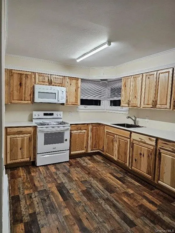 Kitchen featuring light countertops, white appliances, dark wood-style floors, a textured ceiling, and ornamental molding Kitchen featuring light countertops, white appliances, dark wood-style floors, a textured ceiling, and ornamental molding