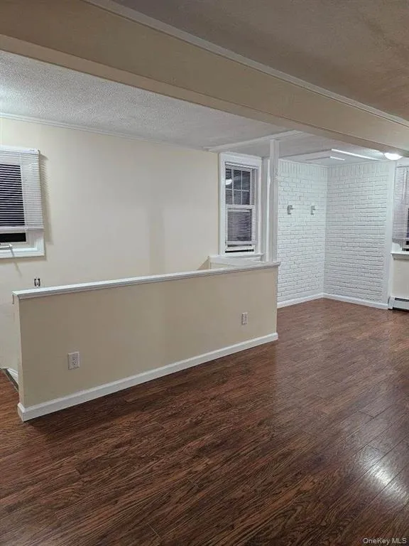 Empty room with ornamental molding, dark wood-style floors, brick wall, and baseboard heating Empty room with ornamental molding, dark wood-style floors, brick wall, and baseboard heating