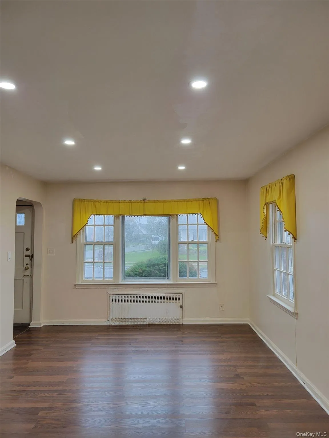 Unfurnished room featuring arched walkways, recessed lighting, plenty of natural light, radiator, and dark wood-style flooring Unfurnished room featuring arched walkways, recessed lighting, plenty of natural light, radiator, and dark wood-style flooring