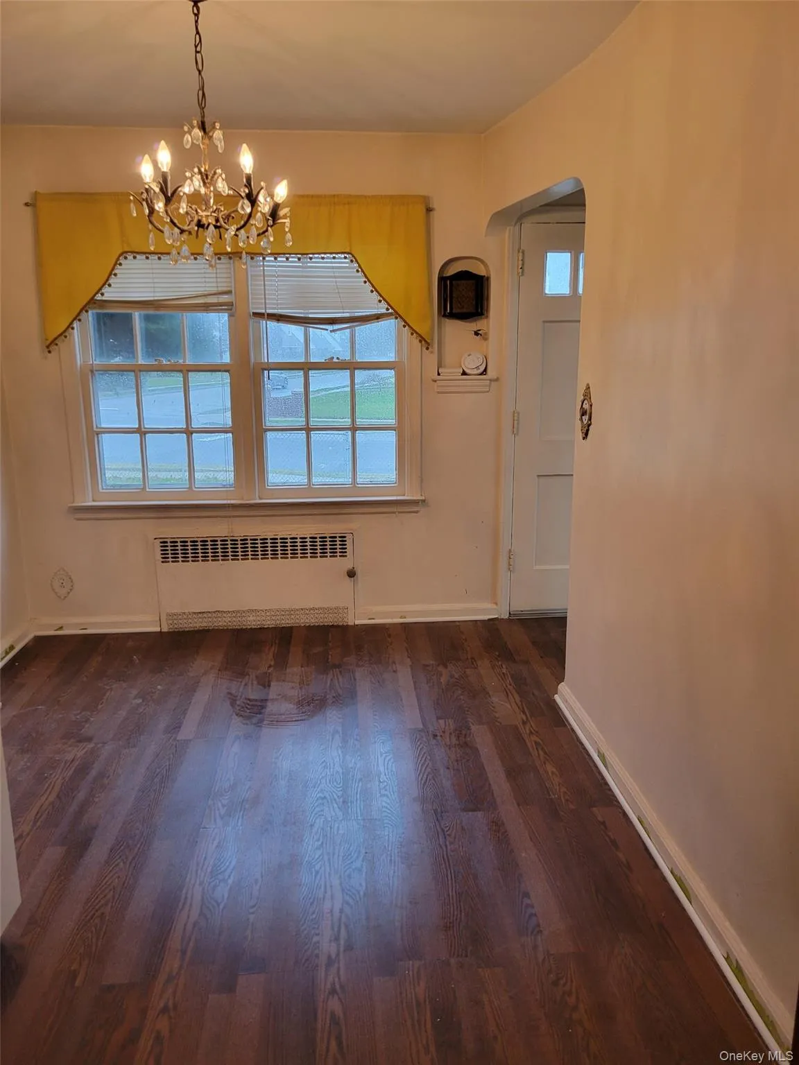 Unfurnished dining area featuring plenty of natural light, radiator, dark wood-style flooring, and arched walkways Unfurnished dining area featuring plenty of natural light, radiator, dark wood-style flooring, and arched walkways