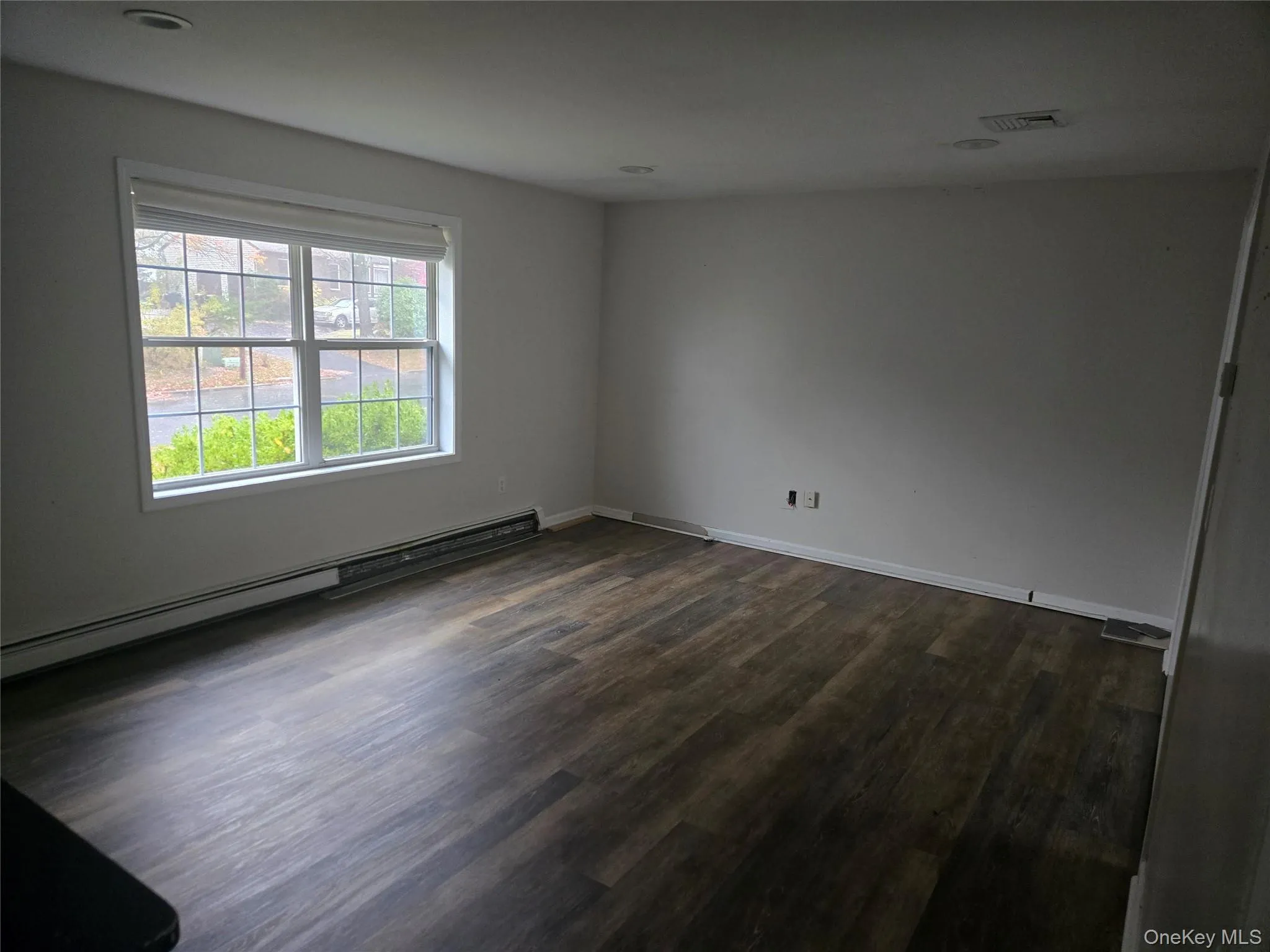 Empty room with baseboard heating and dark wood-type flooring Empty room with baseboard heating and dark wood-type flooring